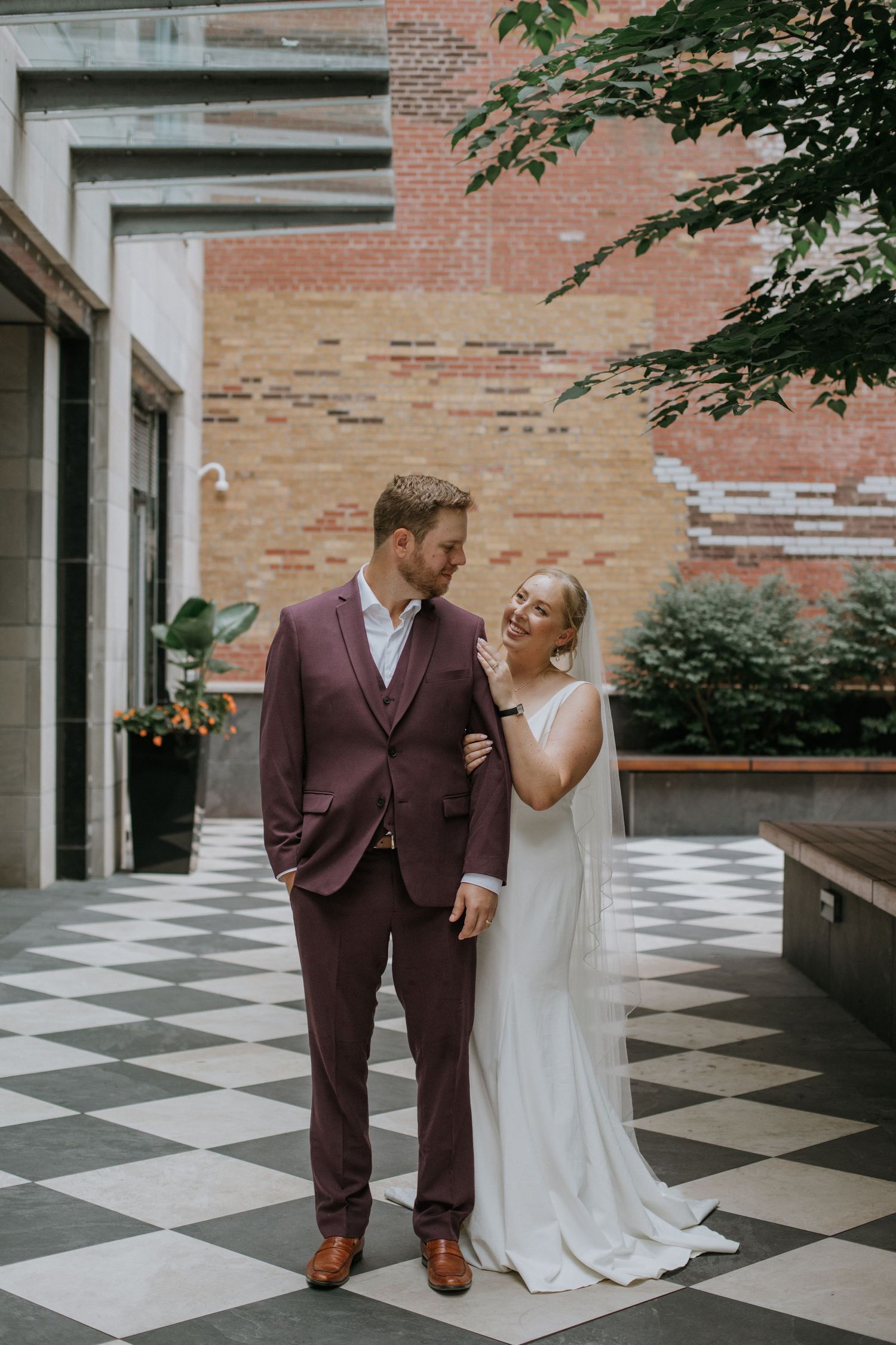 Modern wedding portrait featuring a chic couple on a checkered floor against an industrial brick backdrop.