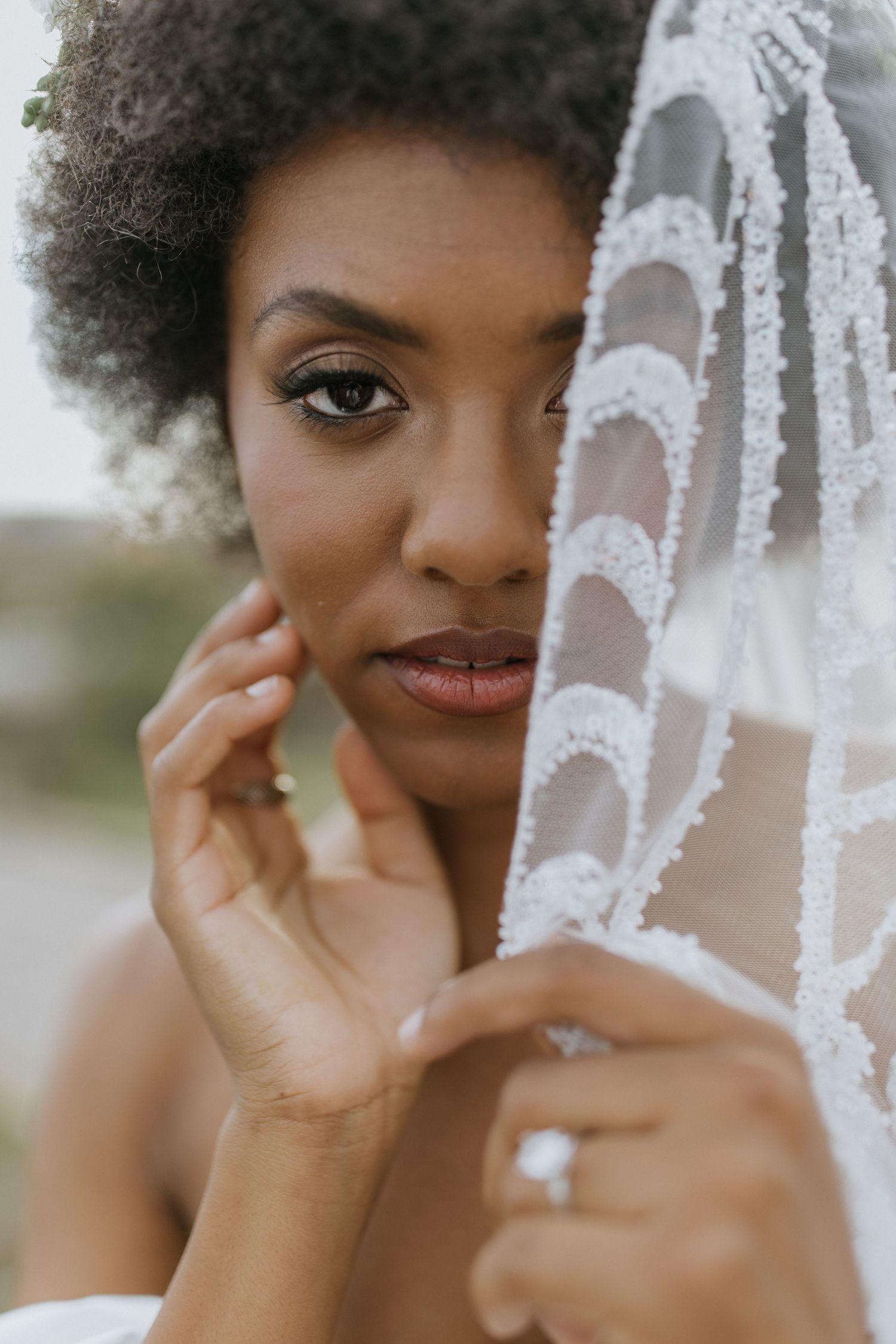 Close-up portrait through delicate lace veil with soft natural lighting.