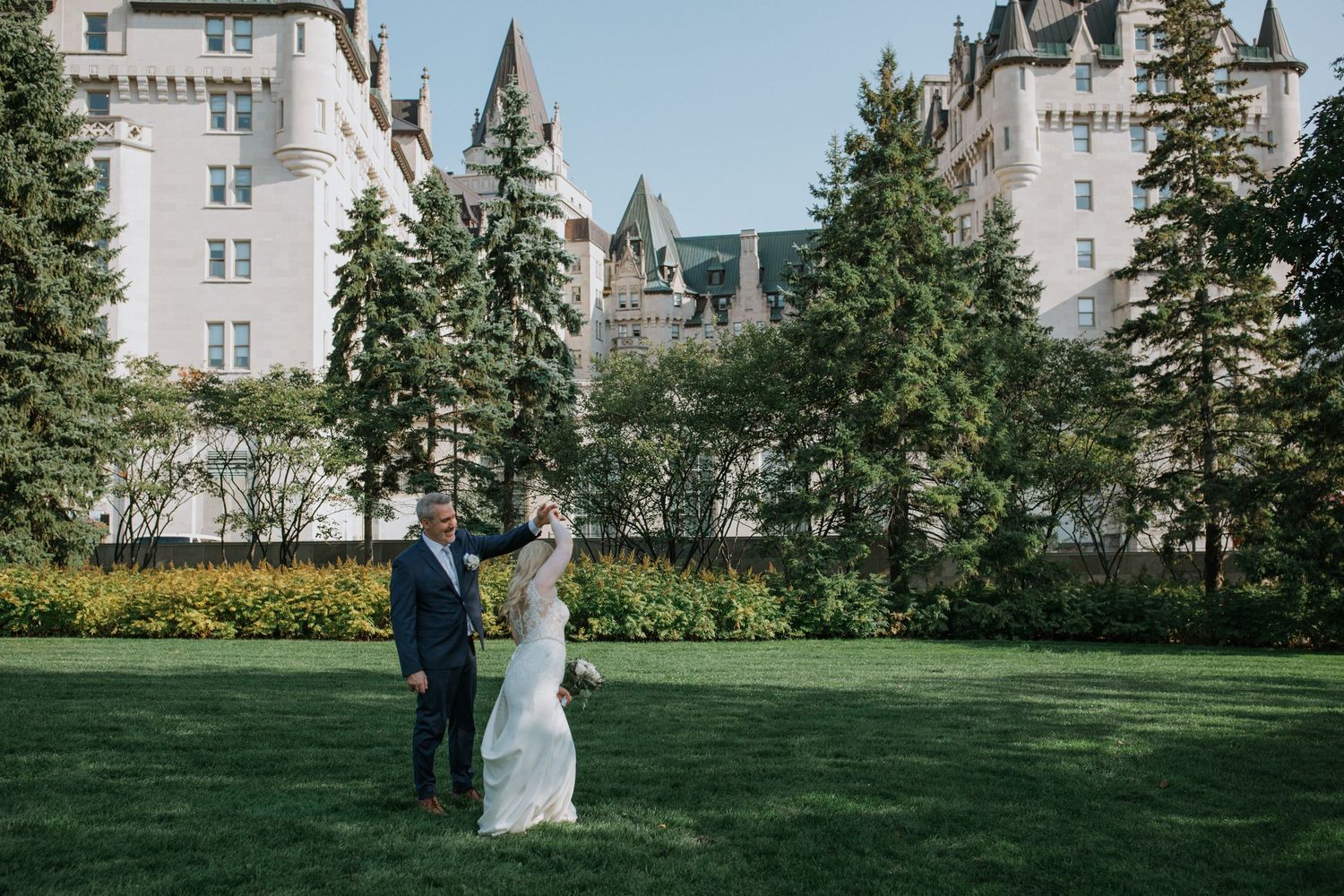 Newlyweds pose in front of a stunning fairytale-like castle with manicured grounds and classic architecture.