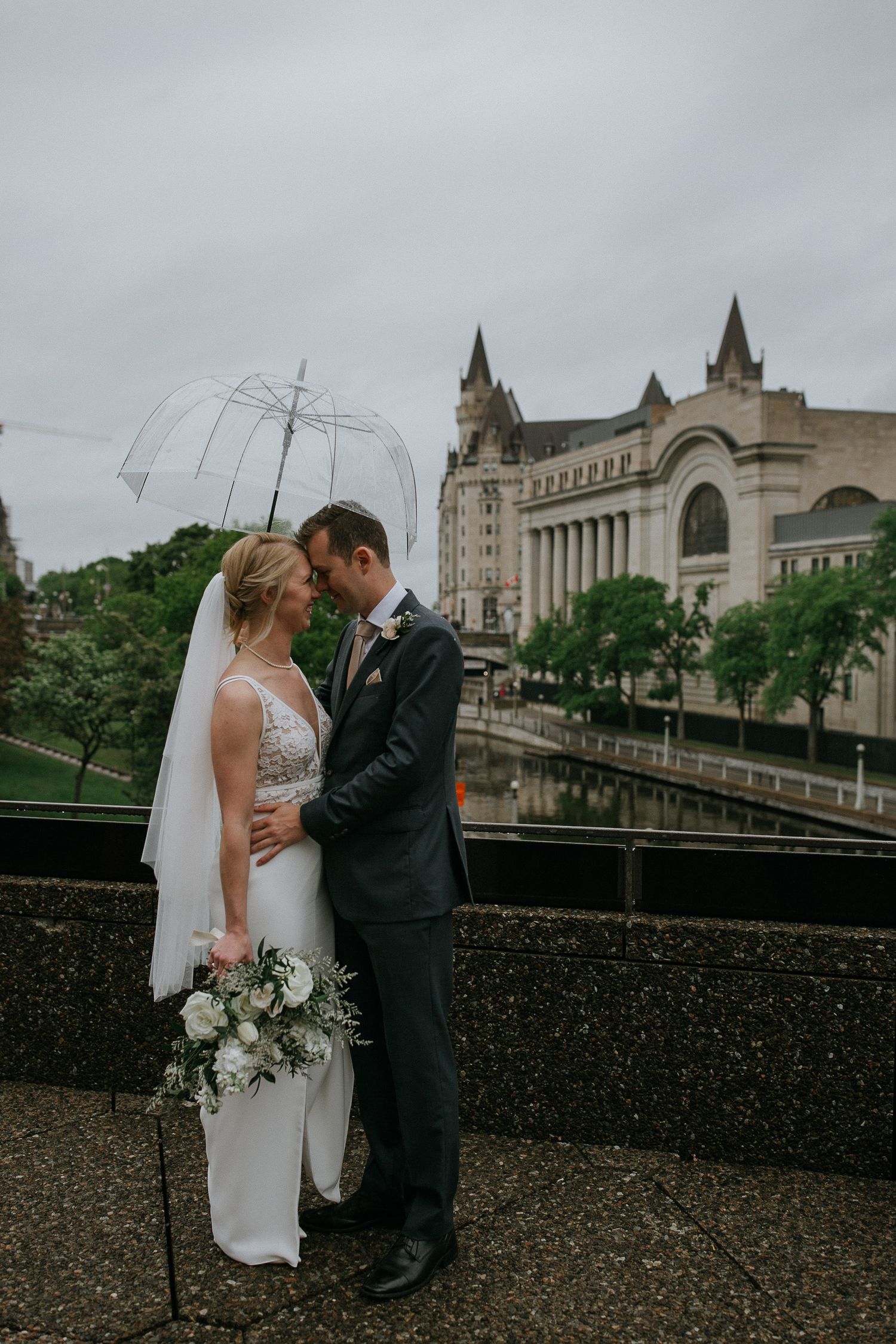 A romantic couple shares a moment against an urban backdrop with historic architecture.