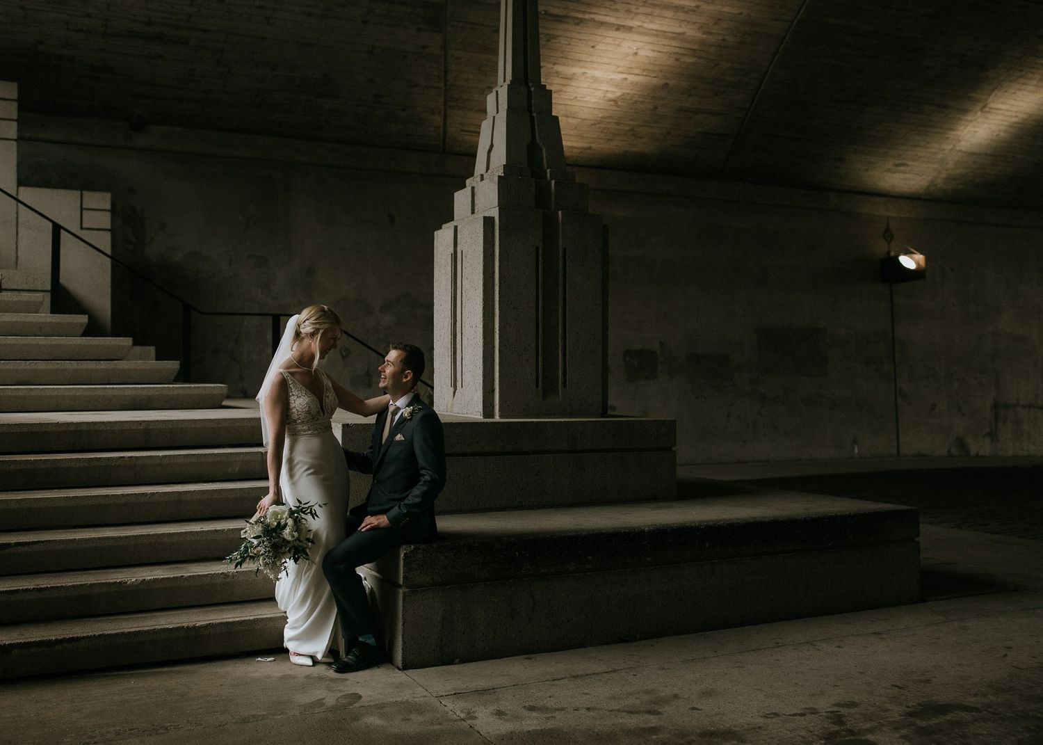 A dramatic wedding photoshoot in a dimly lit concrete stairwell.