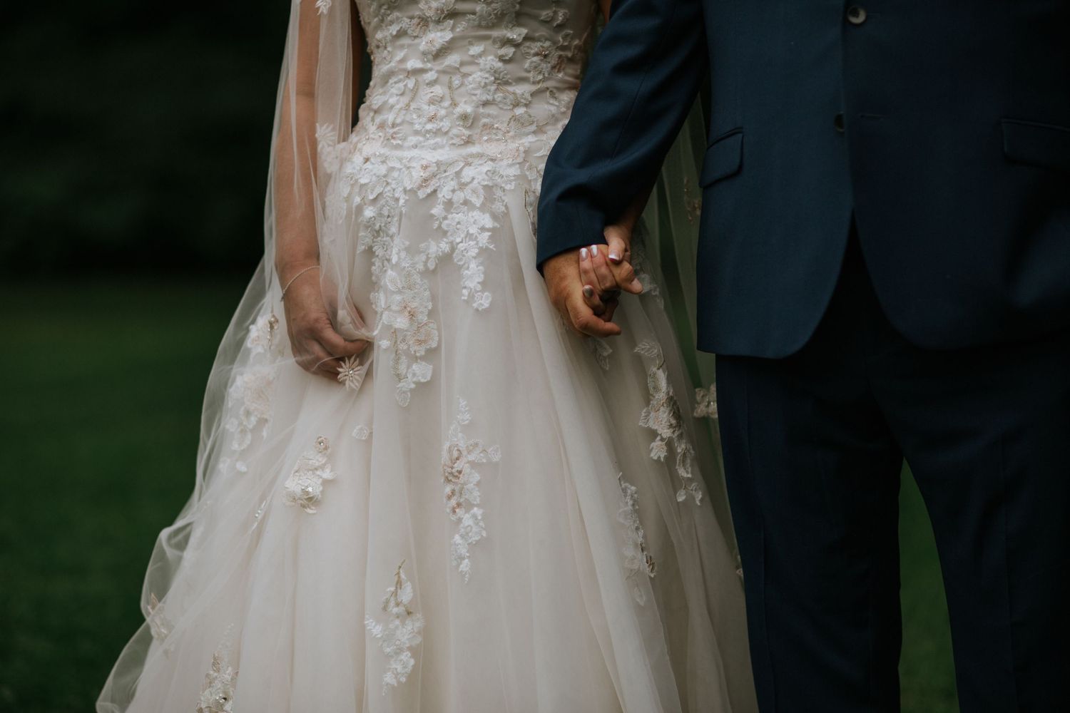 Detail shot of a couple holding hands showing intricate lace details on a wedding dress.