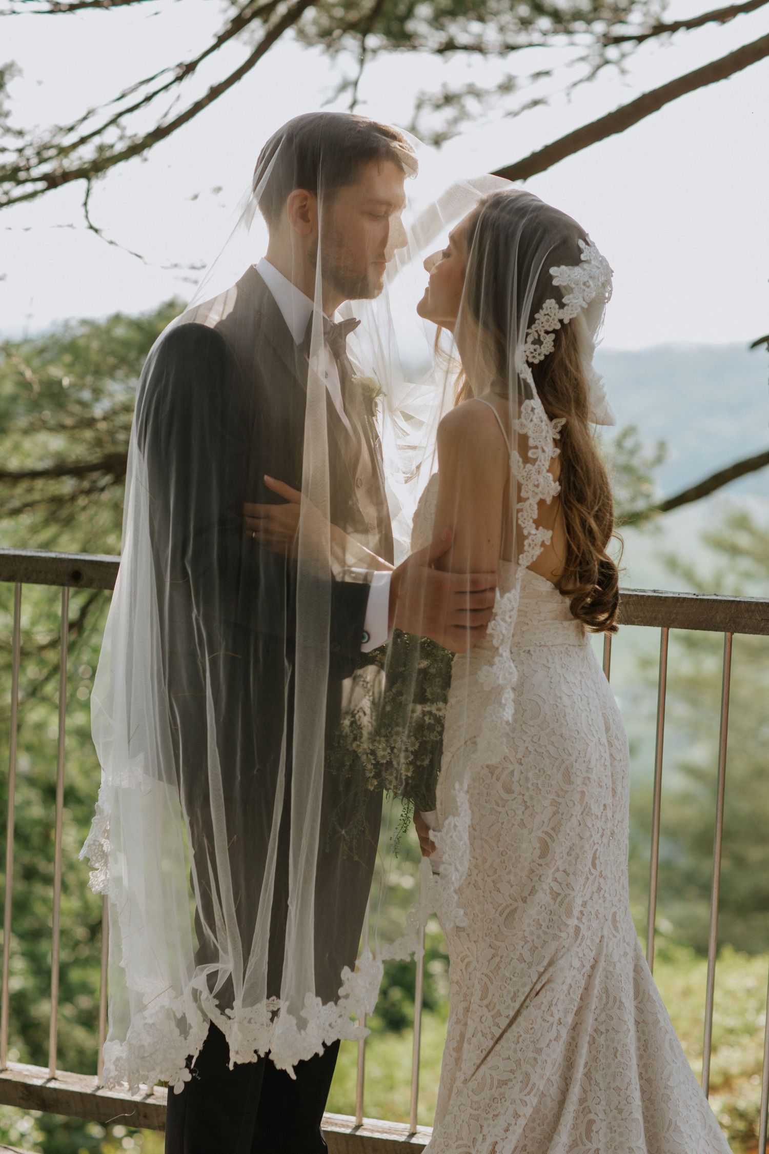 Intimate wedding portrait of couple sharing moment under veil with mountain vista background.