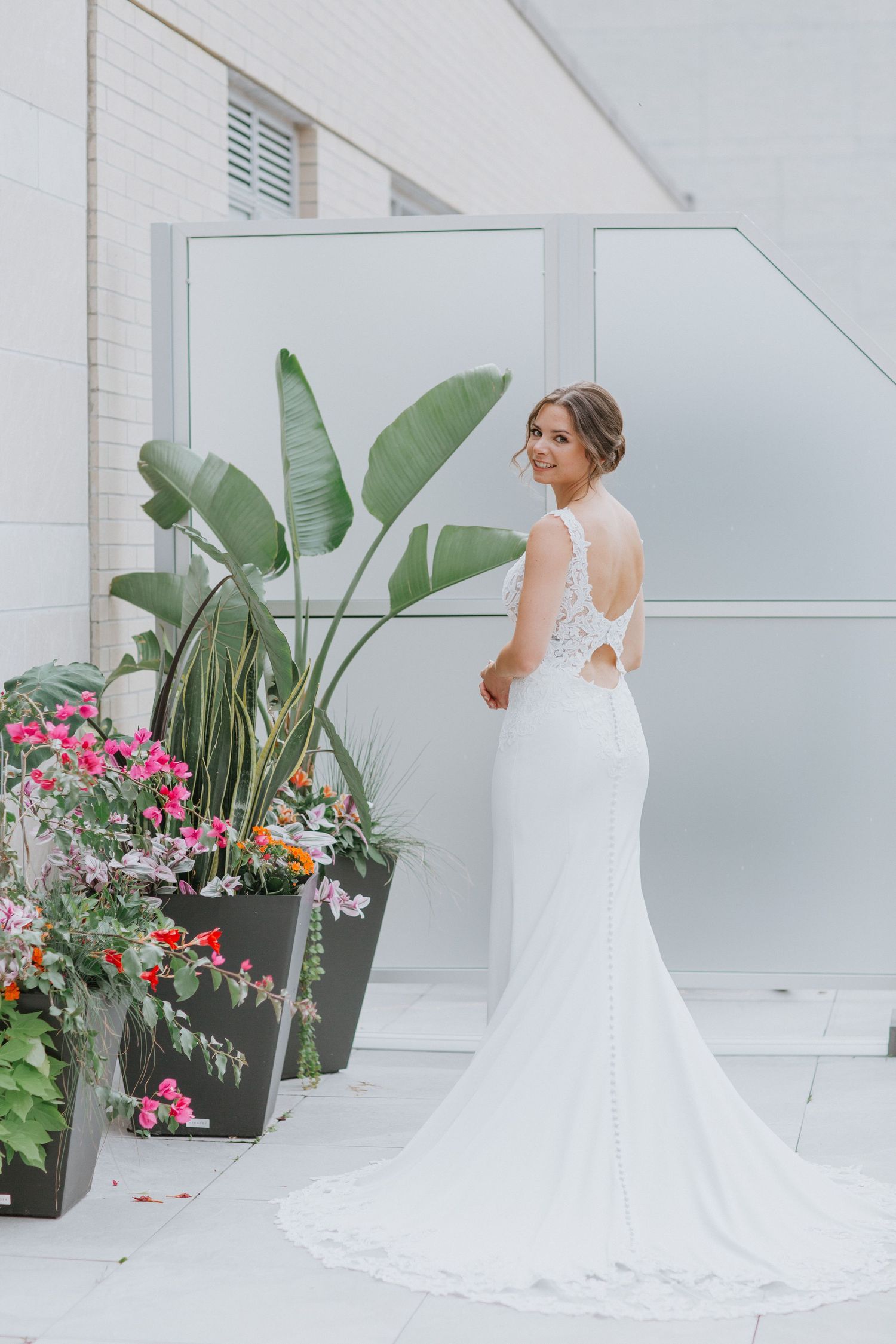 Bridal portrait showcasing lace wedding dress against modern white wall with tropical plants.