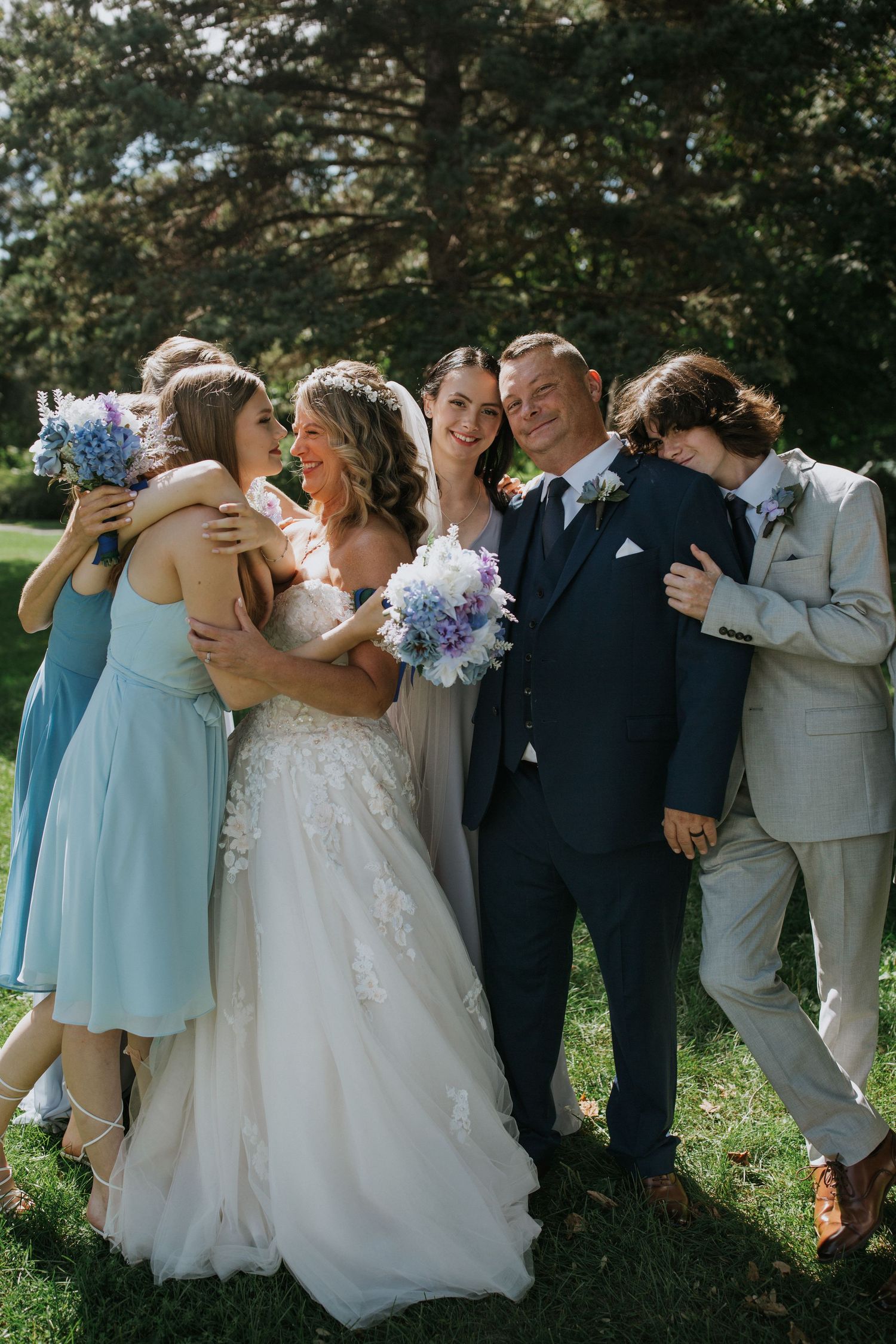 Joyful wedding party in blue and neutral tones laughing together on a sunny lawn.