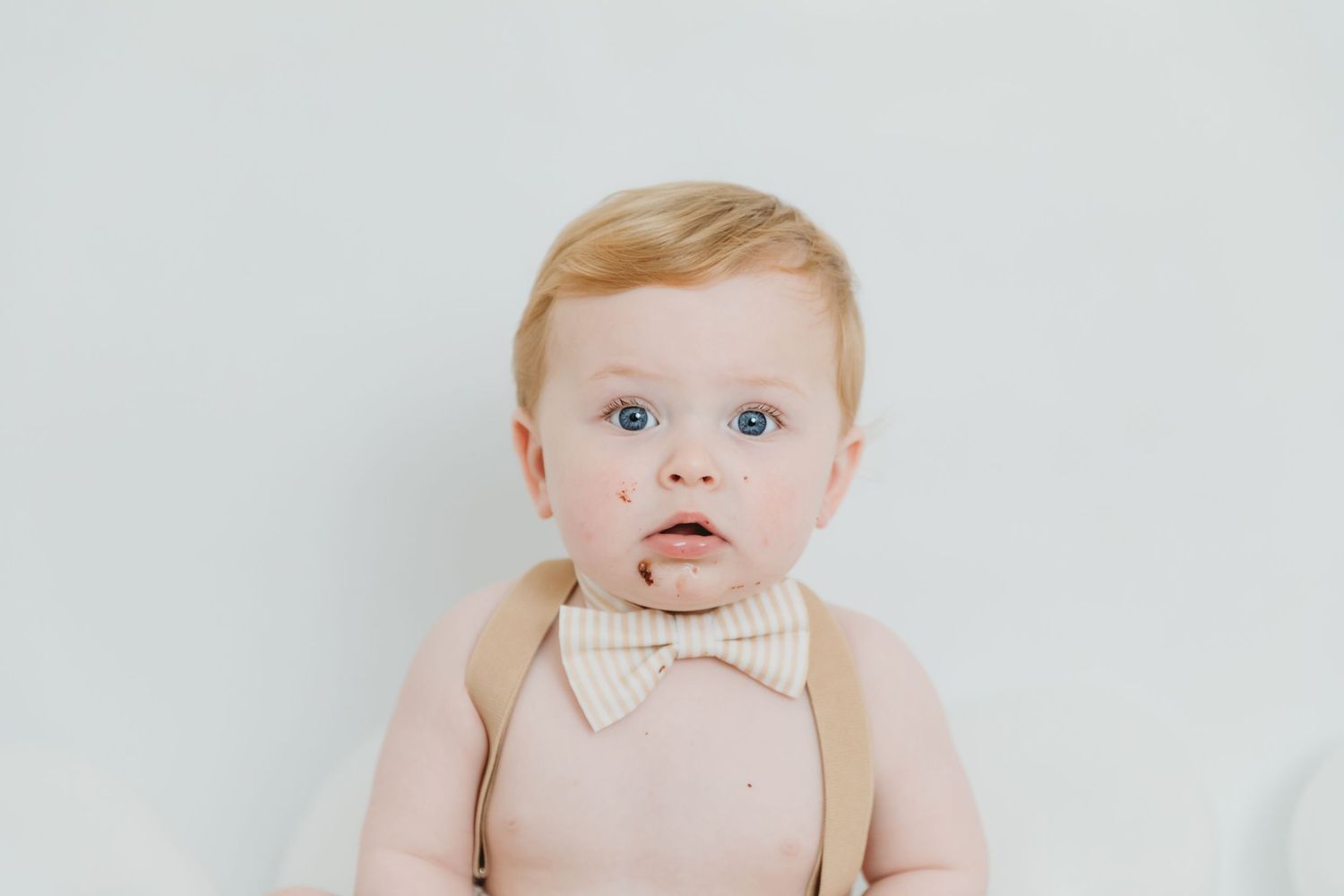 Close-up studio portrait of baby in beige bow tie against white background.