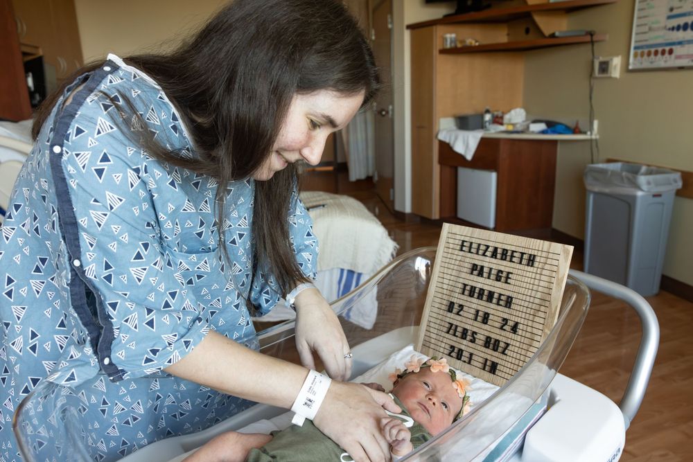 A woman in a floral dress tends to a newborn in a hospital room.