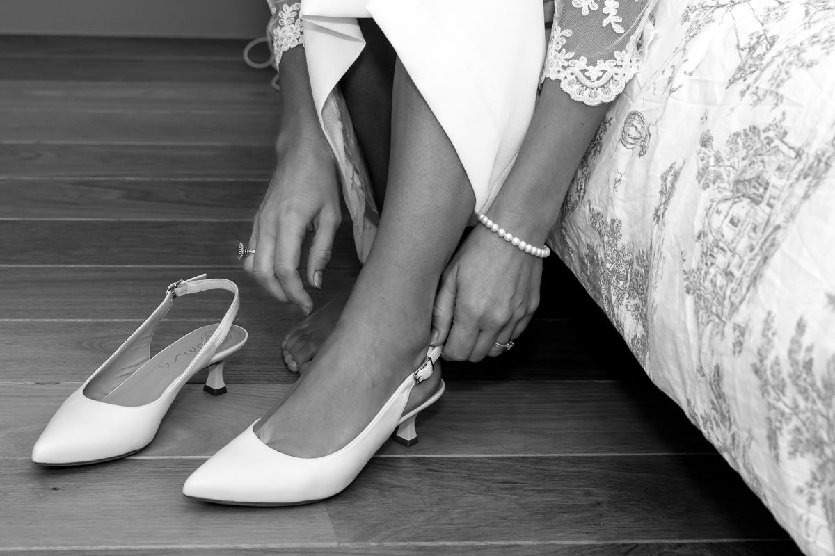 Black and white close-up of bride putting on elegant white slingback heels.