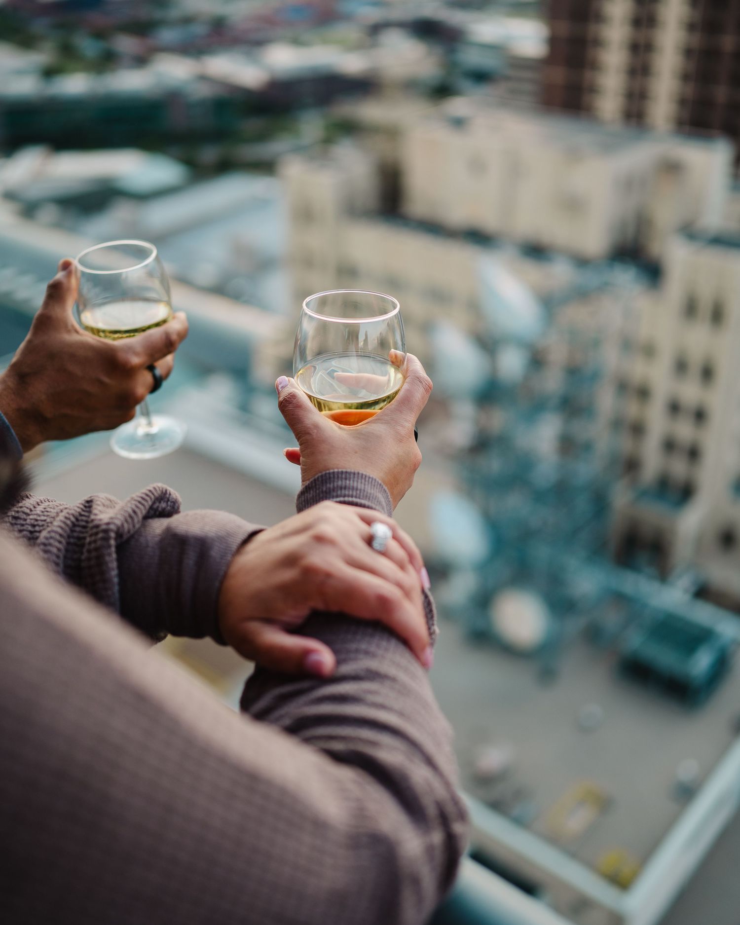 Hands holding wine glasses against a blurred cityscape background at sunset.