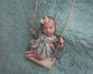 Sweet newborn photo featuring wooden swing prop with mint green textured background.