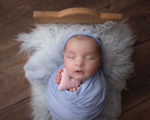 Sleeping newborn wrapped in soft blue fabric on rustic wooden floor with white fur accents.