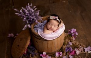 Newborn photography setup with purple flowers and wooden barrel props.