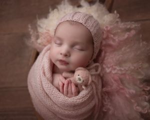 Newborn photography with soft pink wrapping and delicate tulle details on wooden backdrop.
