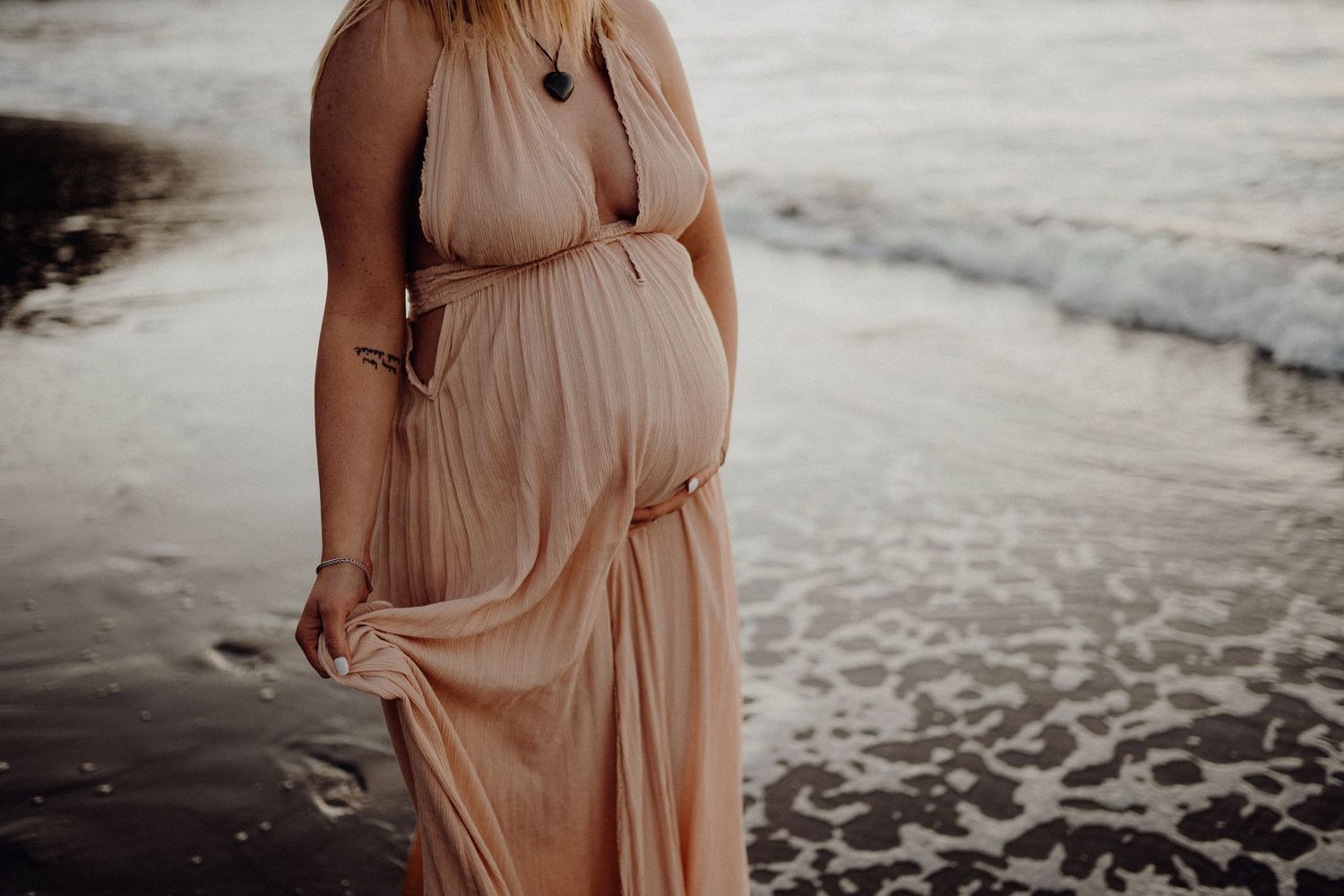 Woman in flowing peach dress walks along beach during golden hour.