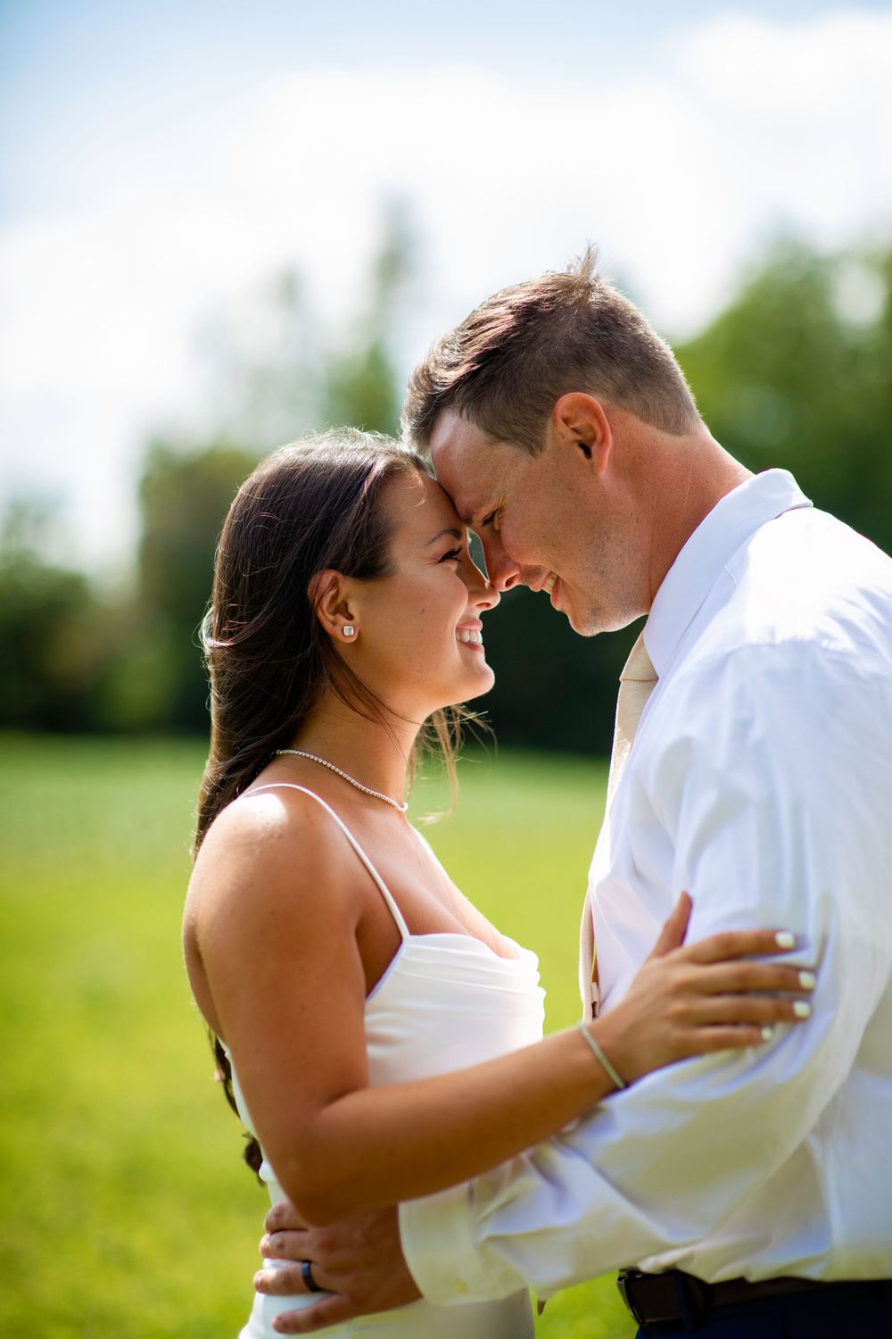 Two people share an intimate romantic moment in a sunny outdoor setting with green foliage in the background.