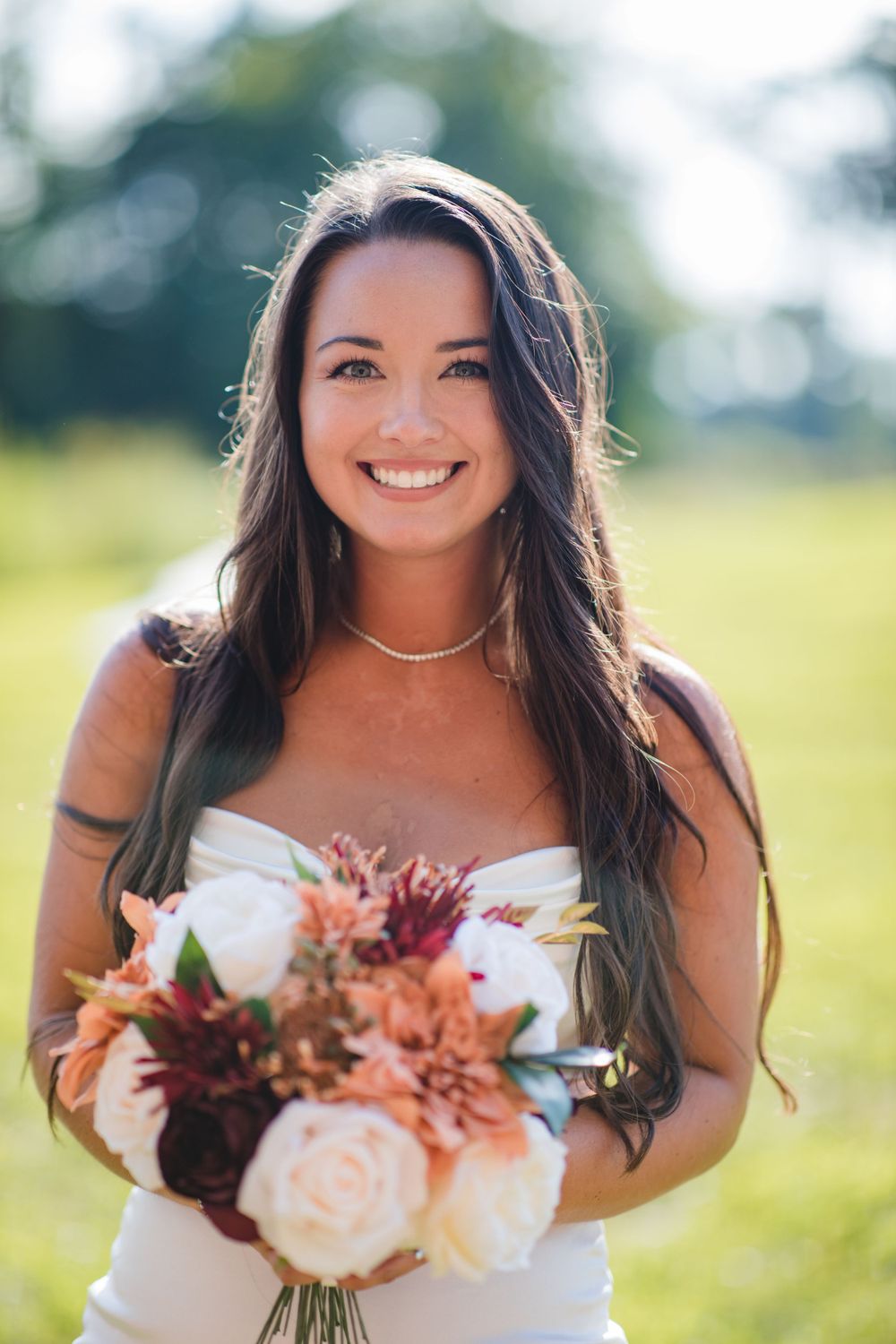 A radiant person in a white dress holds a beautiful bouquet of pink and peach flowers outdoors.