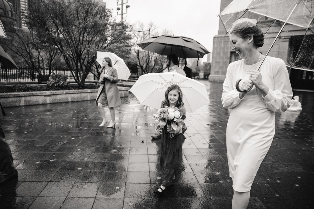 Wedding party walking with clear umbrellas on a rainy day along a stone path.