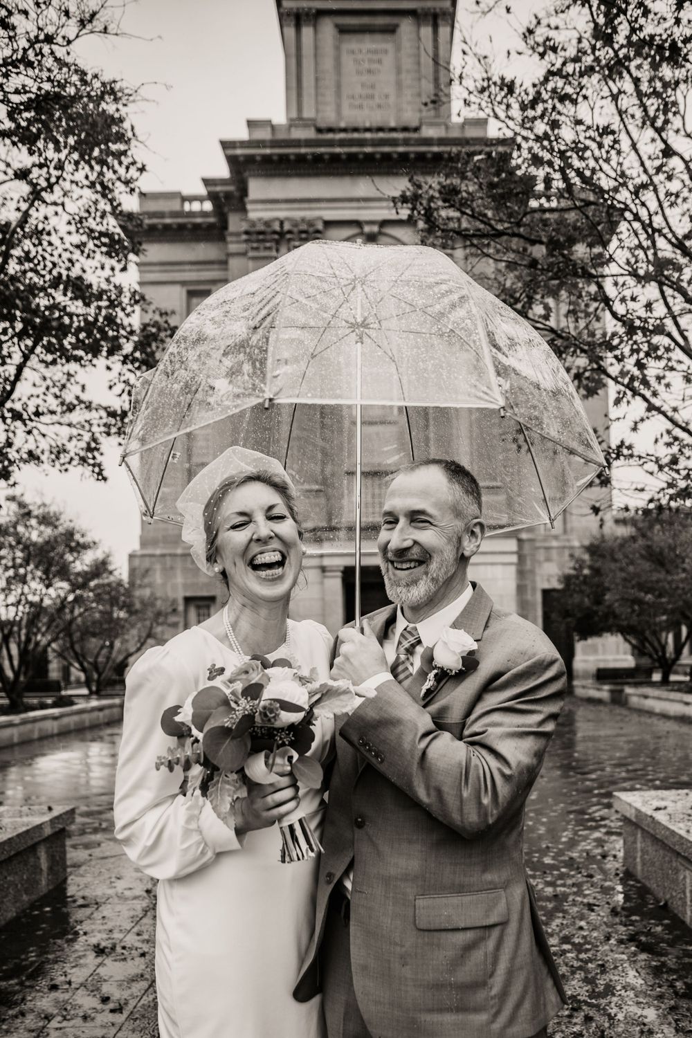 Couple laughing together under a clear umbrella during their outdoor wedding celebration.