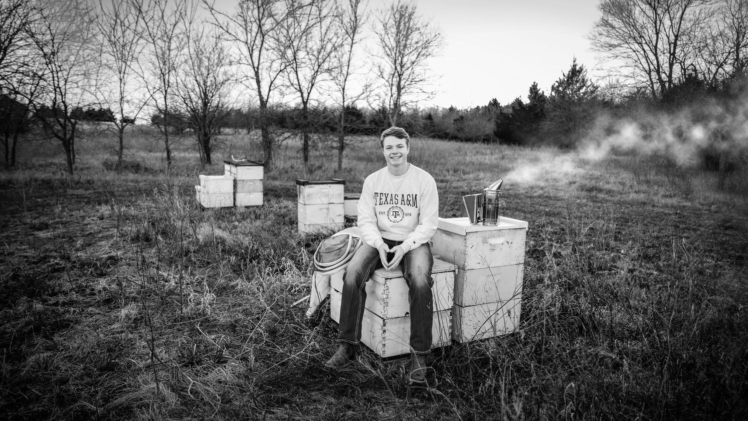 Black and white photo of agricultural equipment and containers arranged in a field at dusk.