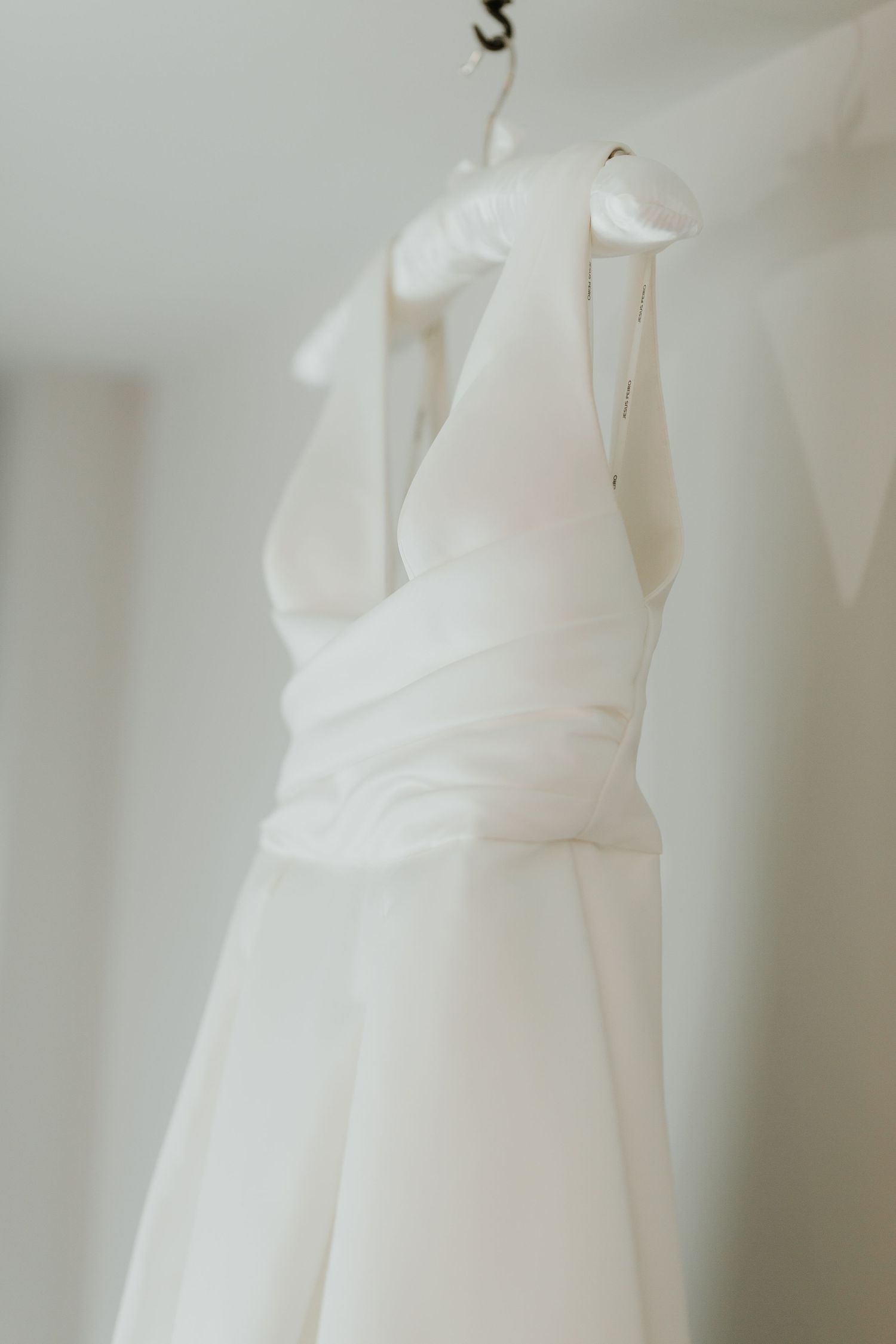 Elegant white wedding dress hanging against light wall.