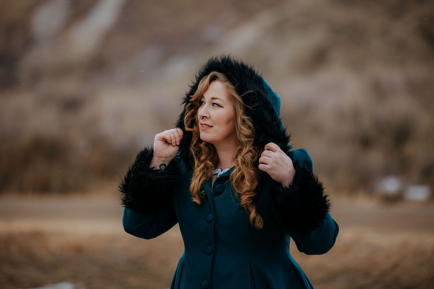 Woman in dark blue winter coat with fur trim hood poses outdoors.