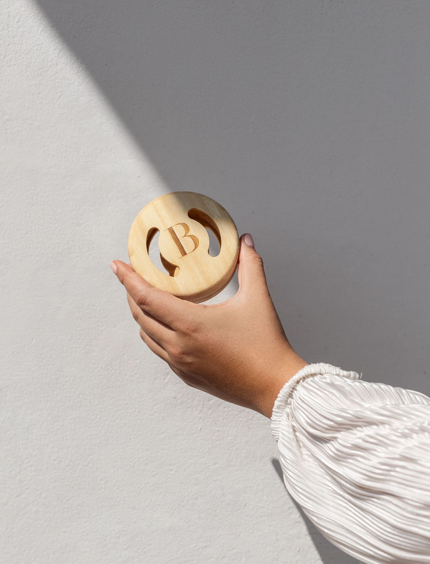 Hand holding a round cream-colored soap with carved design against grey wall.
