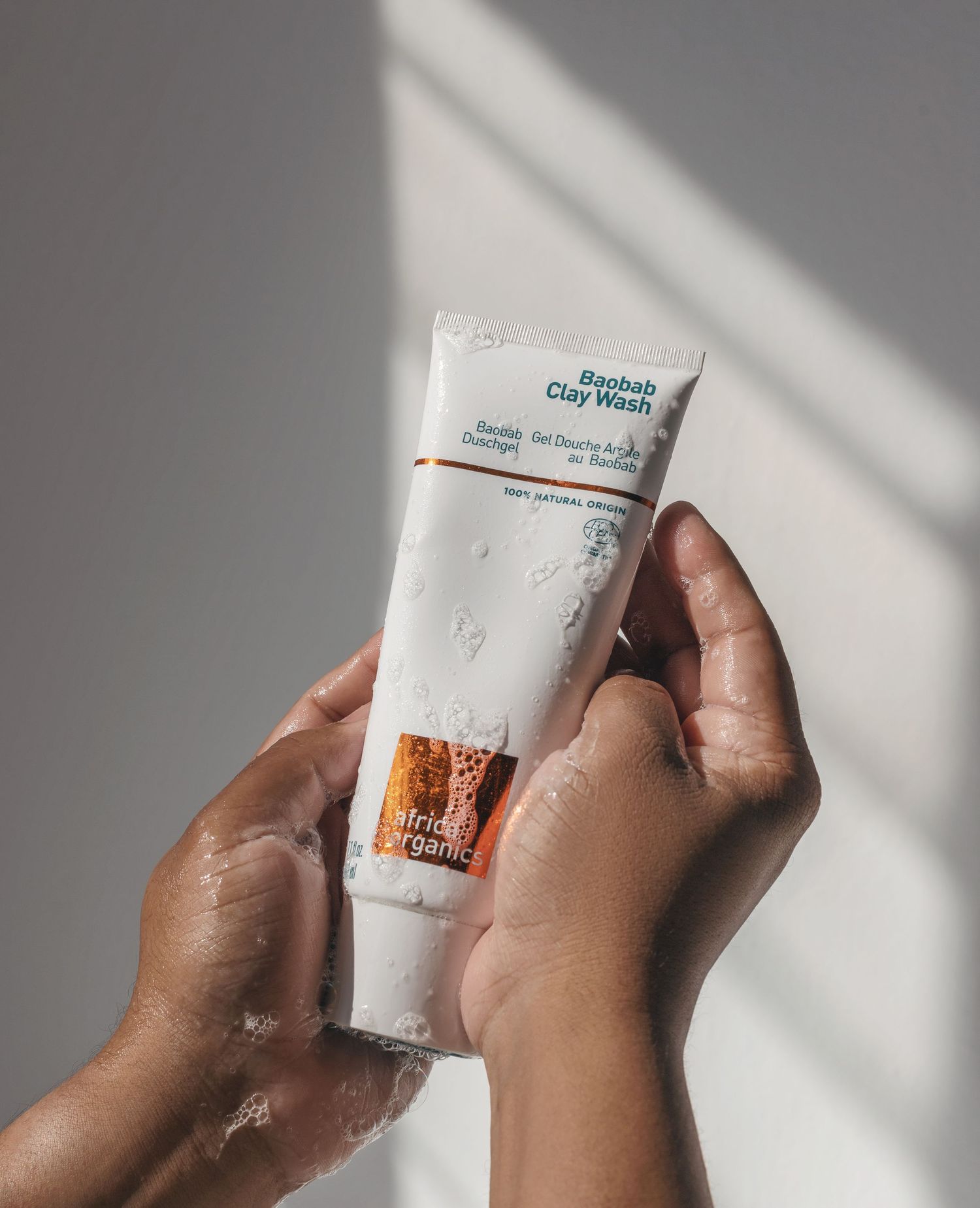 Hands holding and applying white skincare product tube in dramatic lighting.