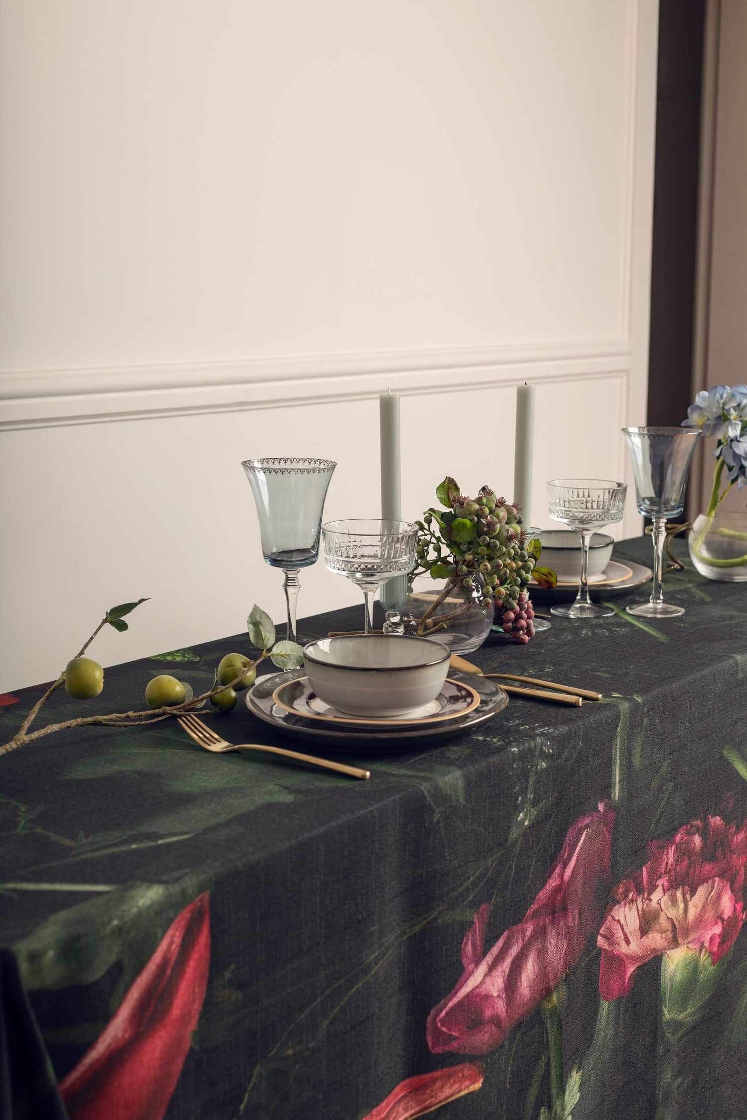 Elegant table setting with blue glassware and floral tablecloth in dark moody lighting.