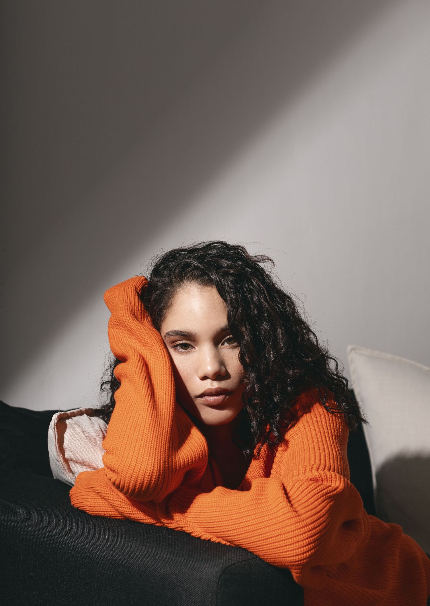 Woman in orange sweater lounging on couch in dramatic lighting.