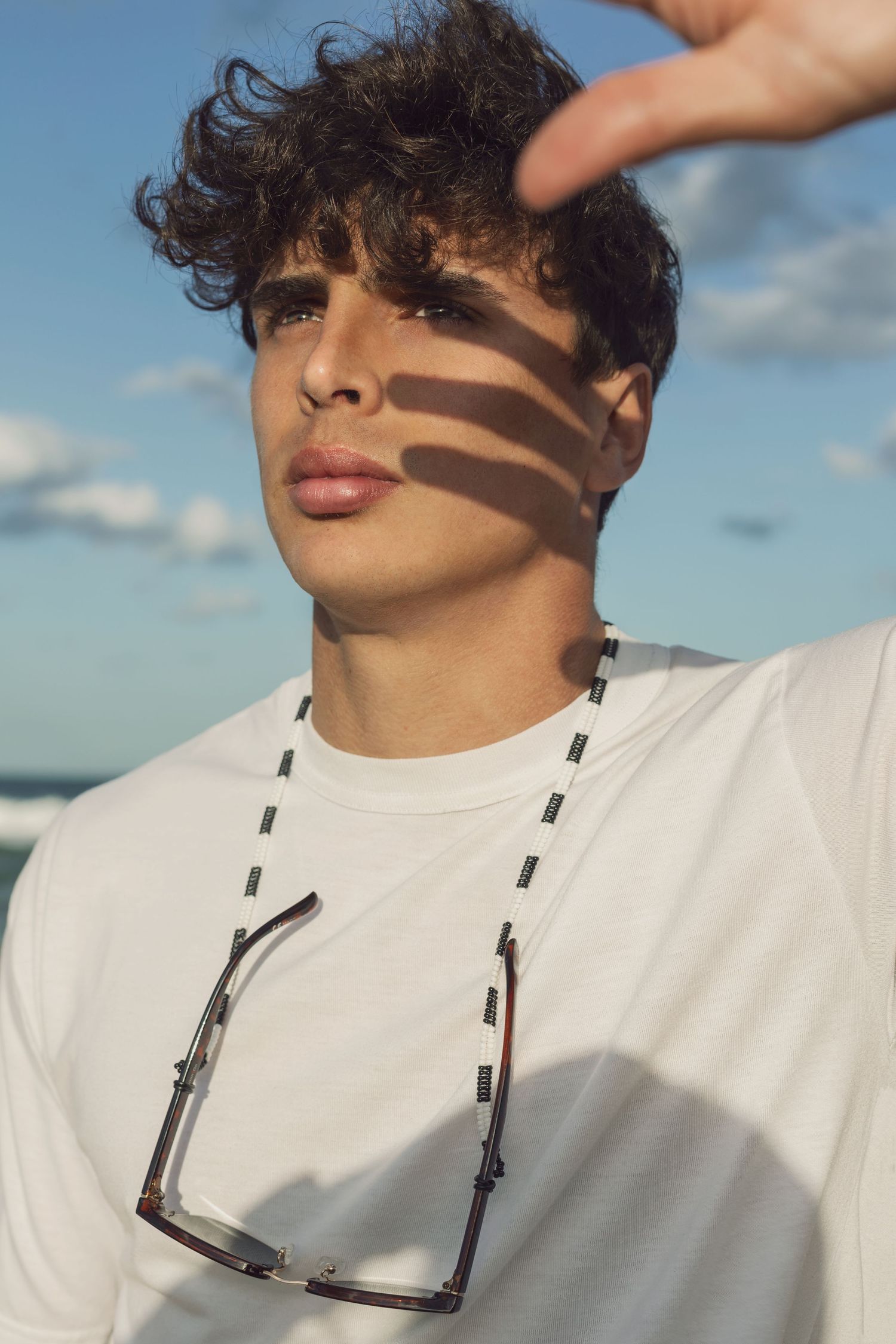 Artistic portrait with sunglasses shadow effect against blue sky background.