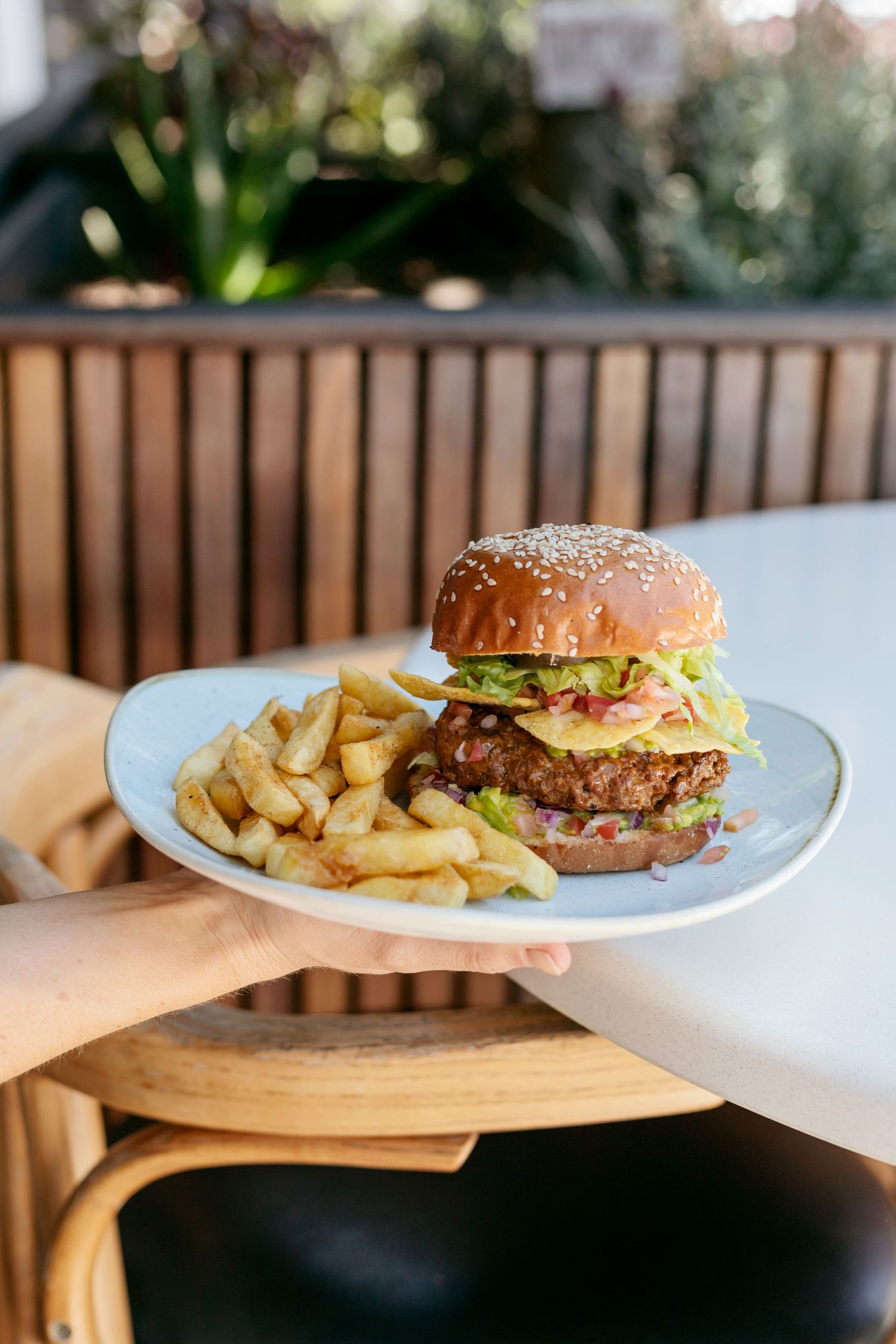 Juicy hamburger and crispy french fries served on a white plate at a wooden table.