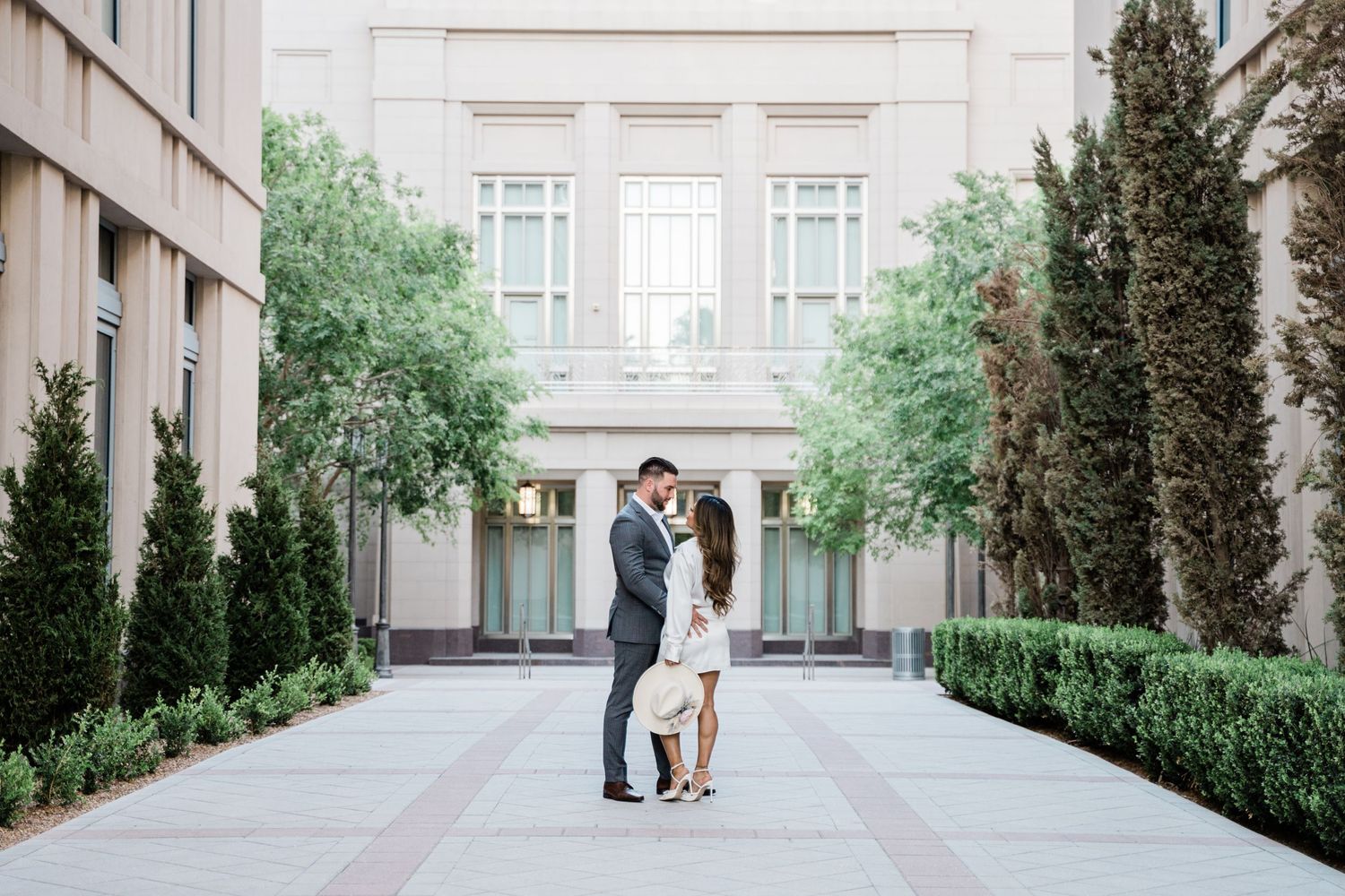 Elegant couple embracing in formal attire in a courtyard with symmetrical architecture.