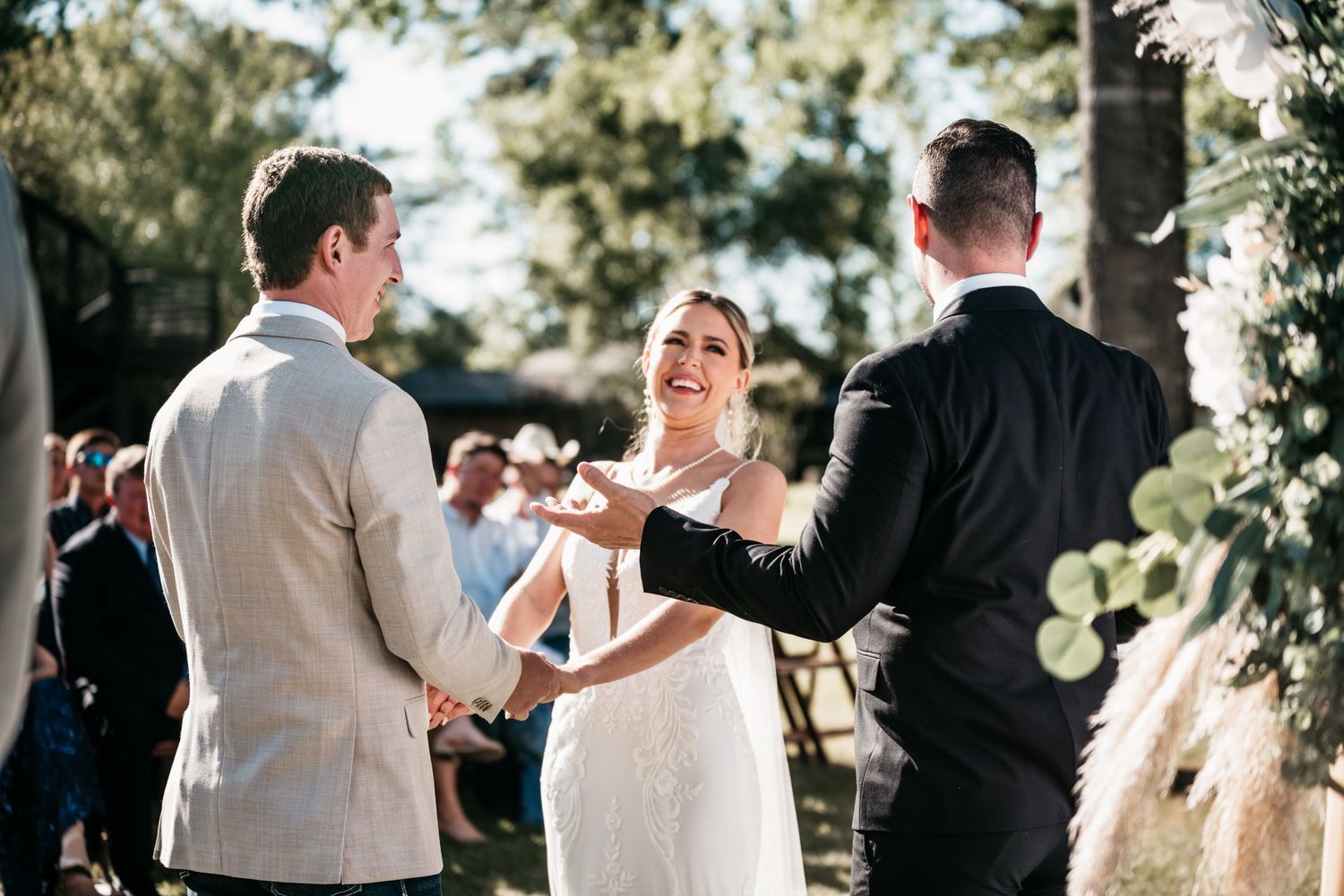 An outdoor wedding ceremony taking place under decorative floral arches.