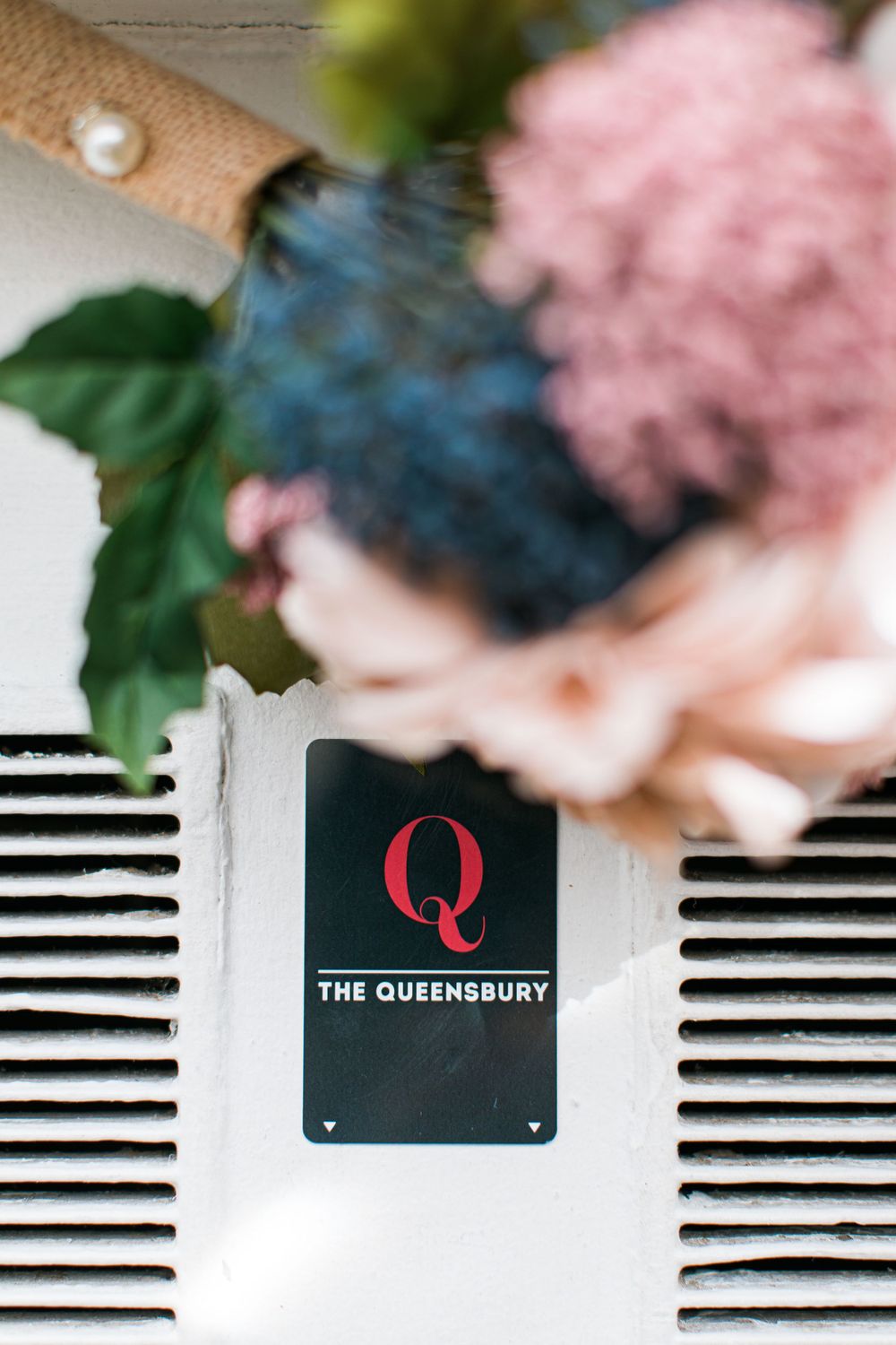 The Queensbury hotel logo sign with pink and blue floral decorations above.