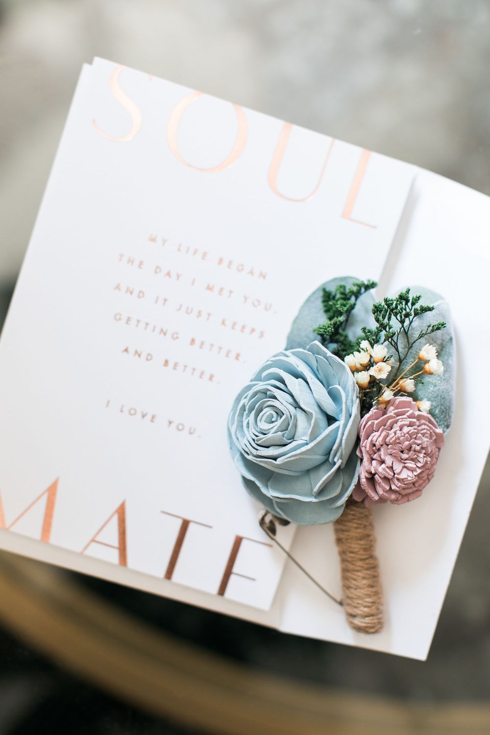 Delicate blue and pink floral boutonniere rests on a wedding invitation.
