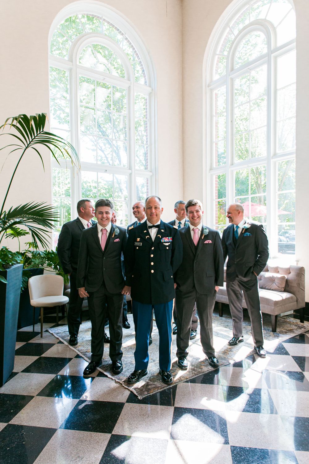 Wedding party members gather in an elegant room with arched windows and checkerboard flooring.