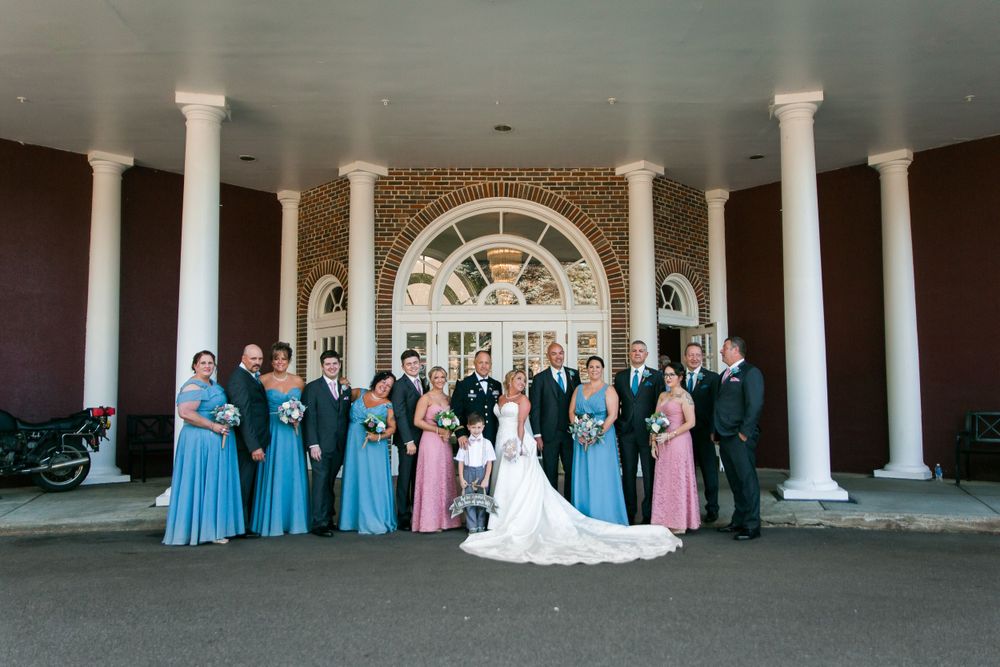 Wedding party in blue and pink dresses poses under columned entrance of venue.