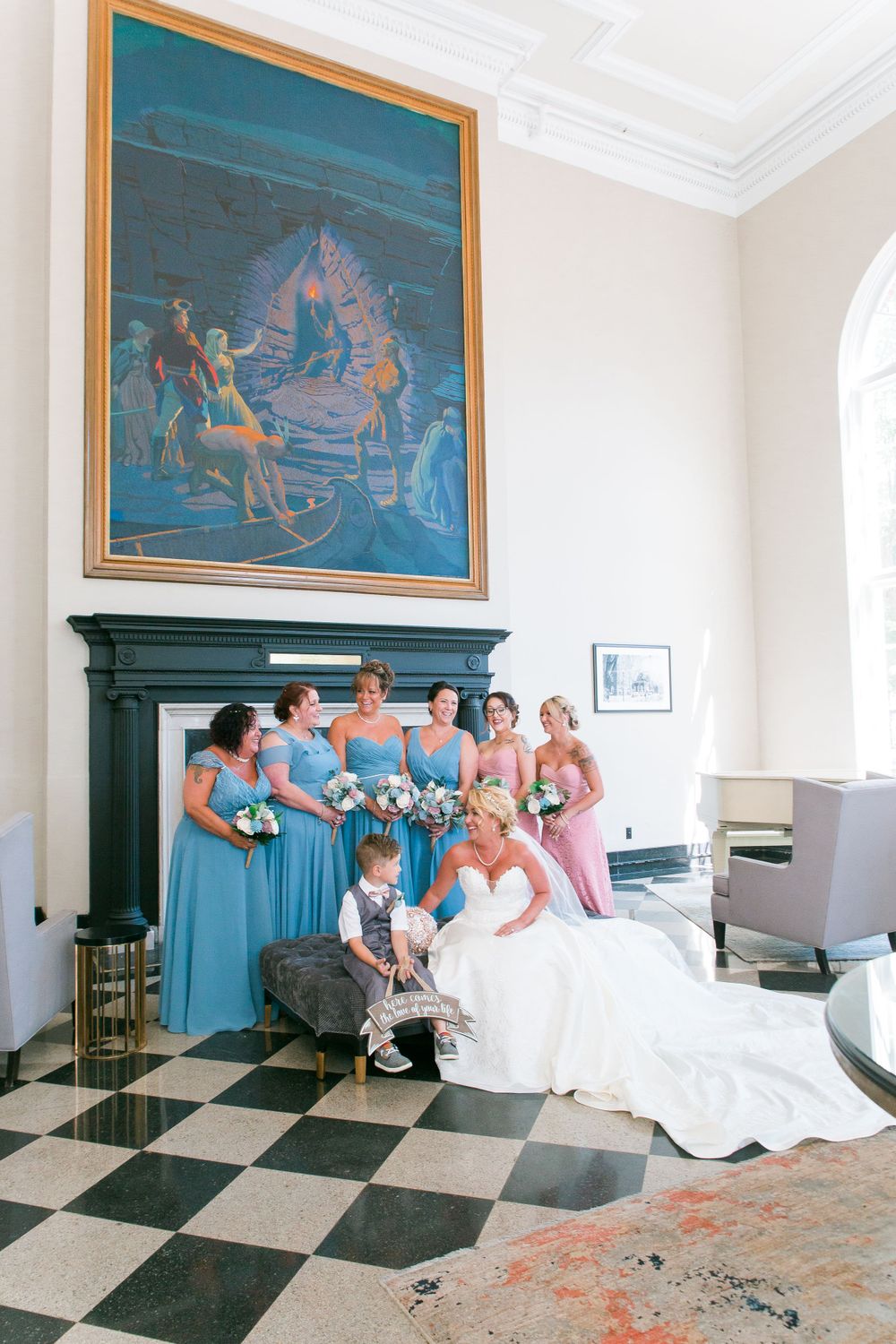 Wedding party poses for photos in front of a large decorative painting in an elegant room.