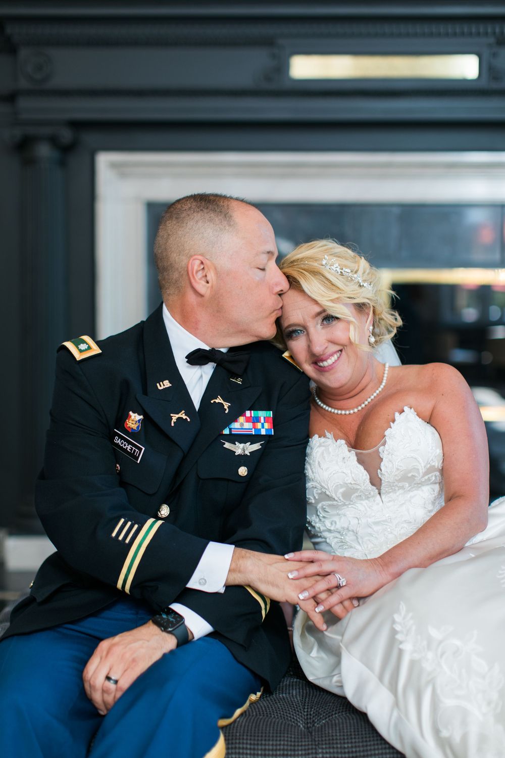 Military officer in dress uniform embraces bride in white gown during intimate moment.