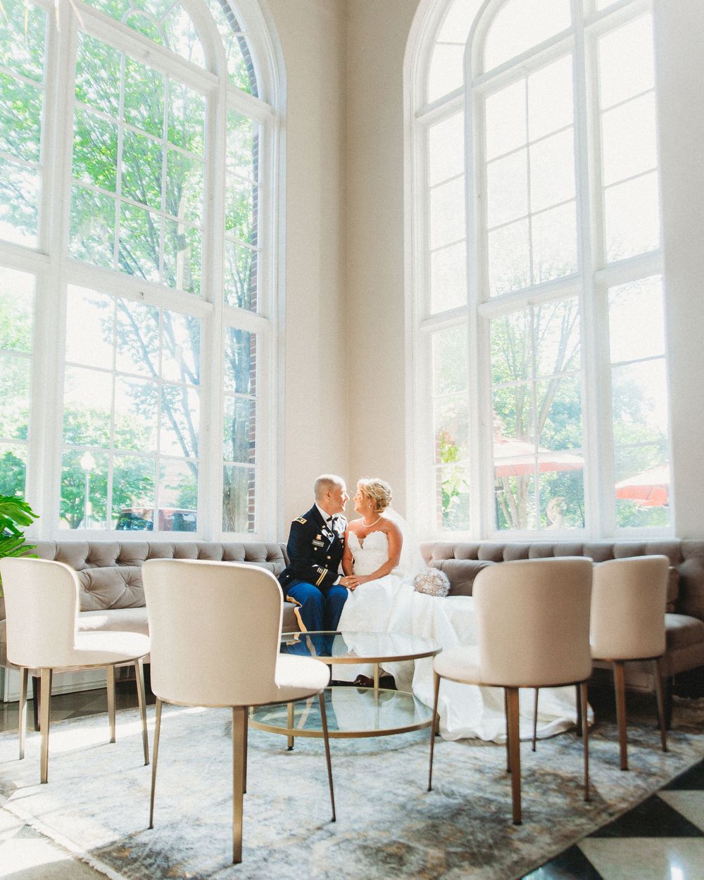 Wedding couple in elegant seating area with tall arched windows and modern furnishings.