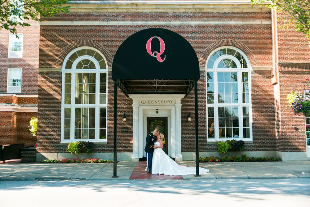 Wedding couple poses under The Queensbury entrance with classic brick and arched windows.
