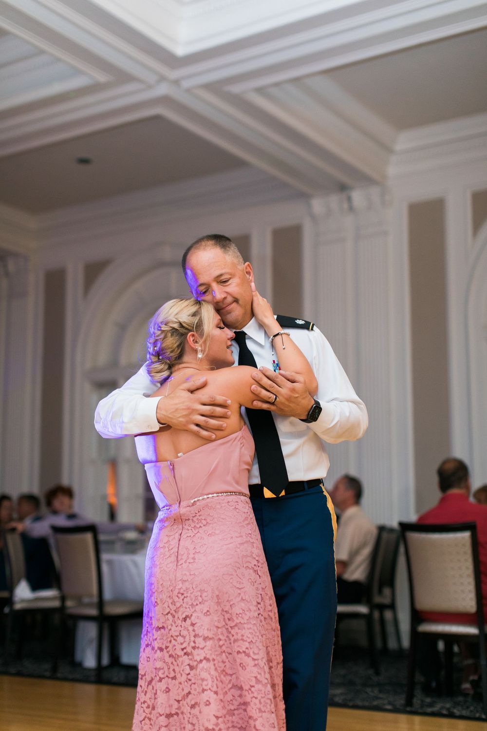 A couple shares an intimate dance moment in an elegant ballroom with ornate white moldings.