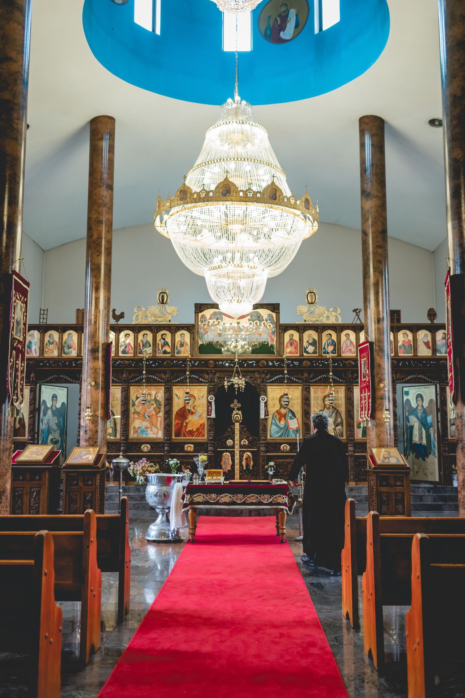 Interior of a church with grand crystal chandelier hanging from a blue domed ceiling.