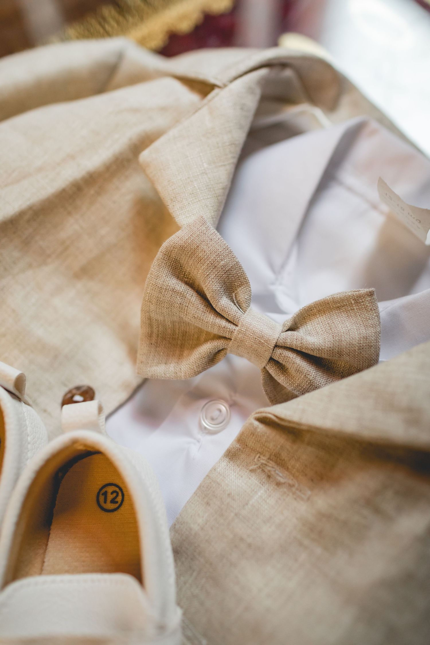 Beige linen bow tie displayed with formal white shirt and dress shoes.