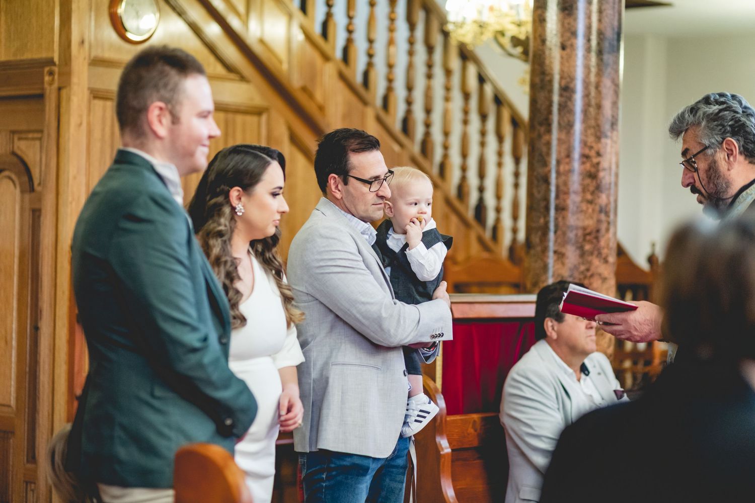 Group gathered for religious ceremony inside historic church with wooden staircase and columns.