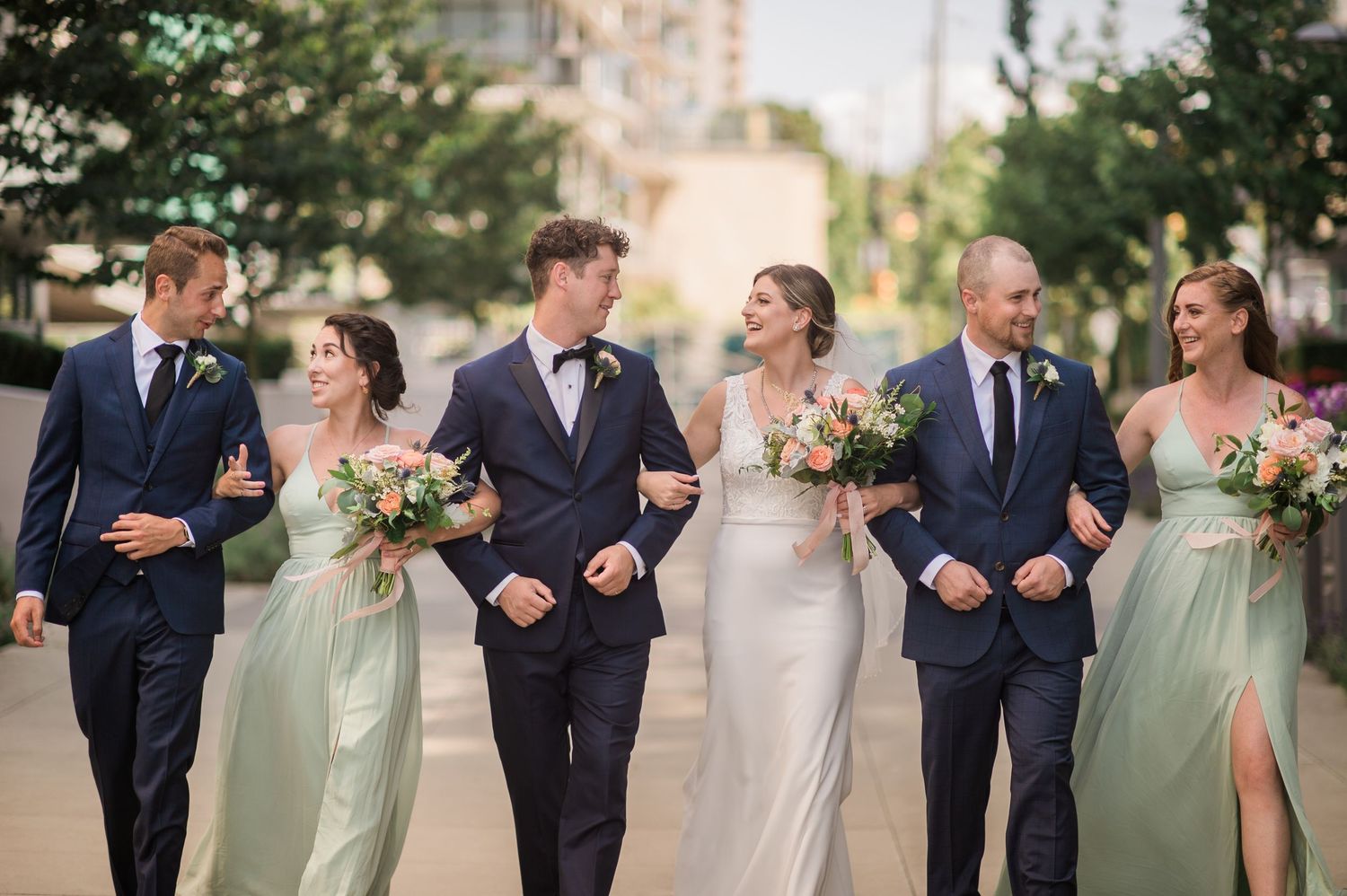 Wedding party walking together with bridesmaids in sage green dresses.