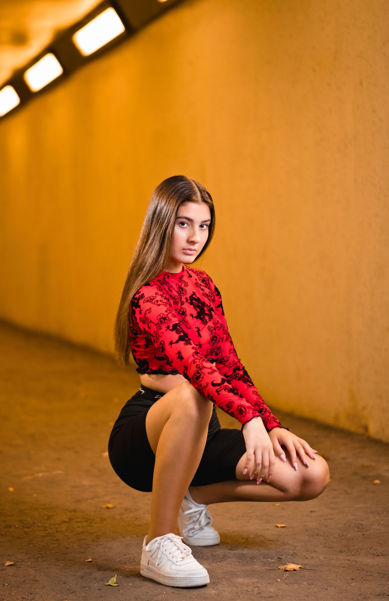 Person in red patterned top and black shorts crouching in urban corridor.
