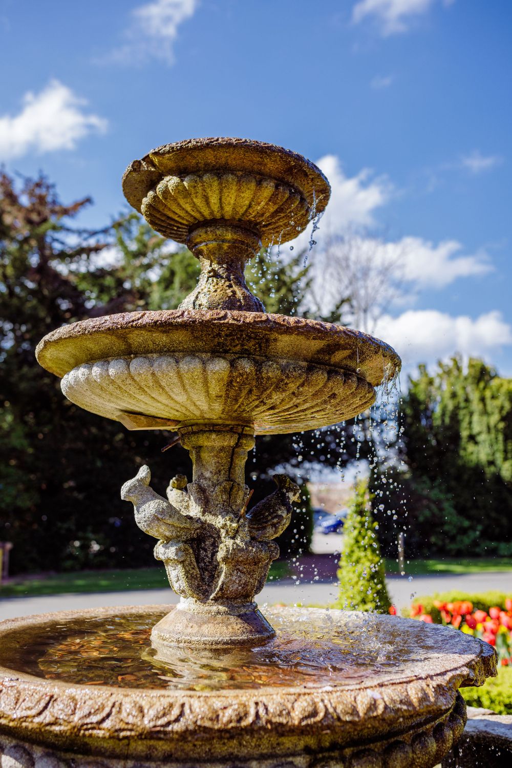 Ornate tiered stone fountain with water spraying in a formal garden setting.