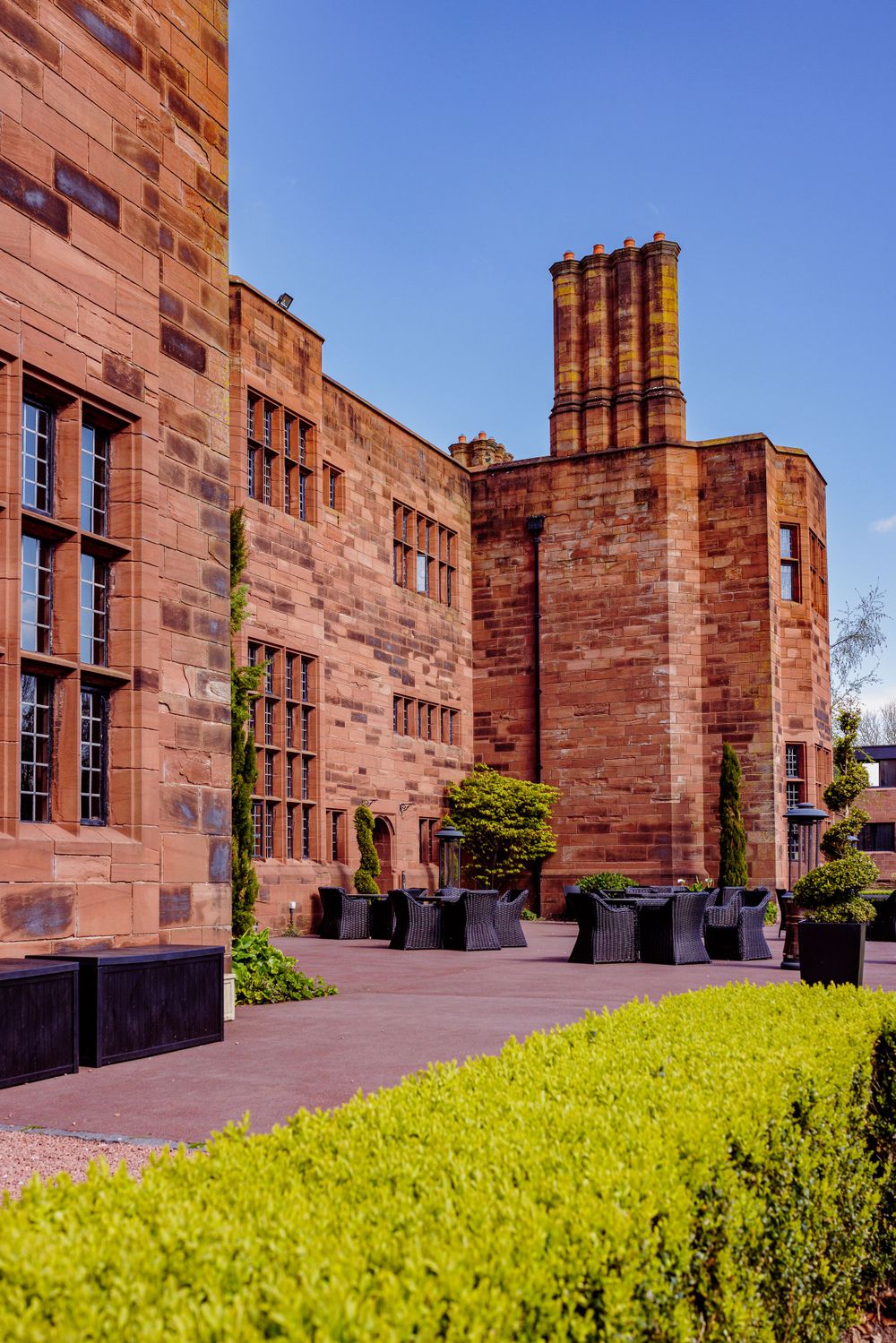 Historic red sandstone building with traditional architecture and manicured hedges.