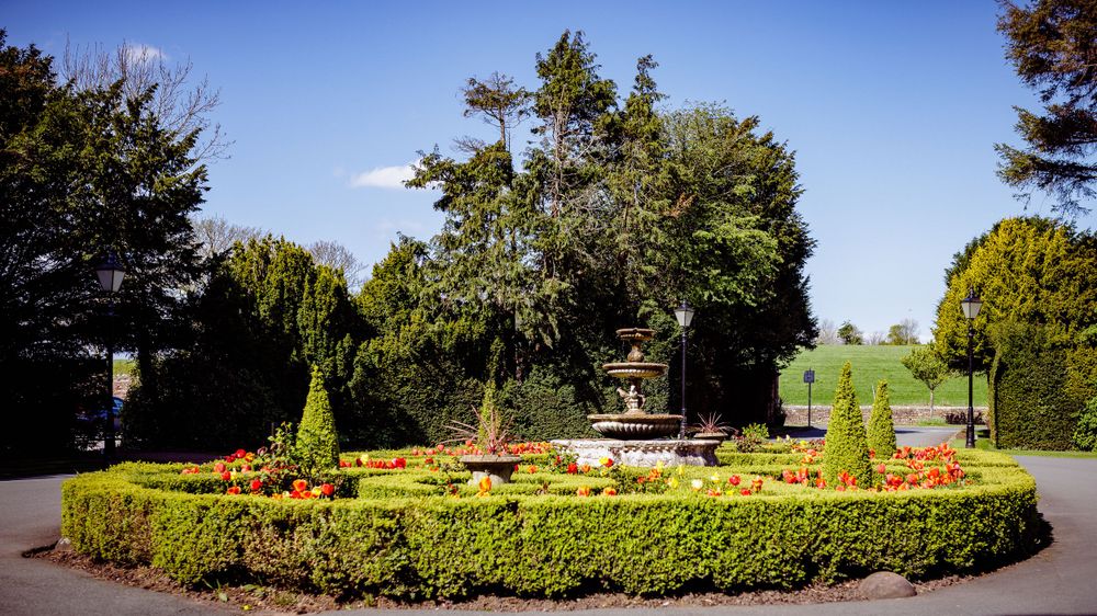 Circular garden with manicured hedges and ornamental features surrounded by evergreen trees.